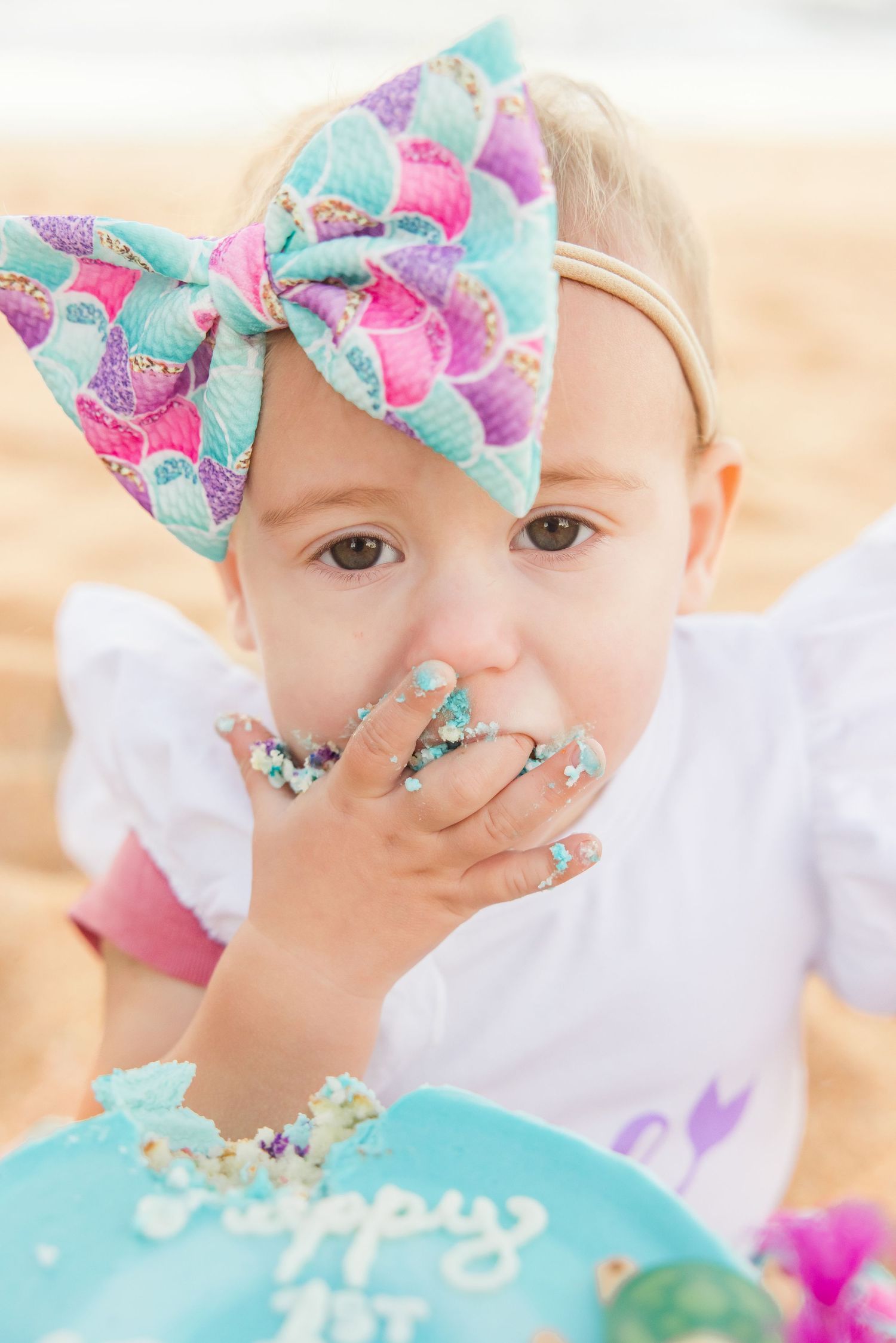 Baby girl with mermaid bow eating cake at first birthday beach smash.