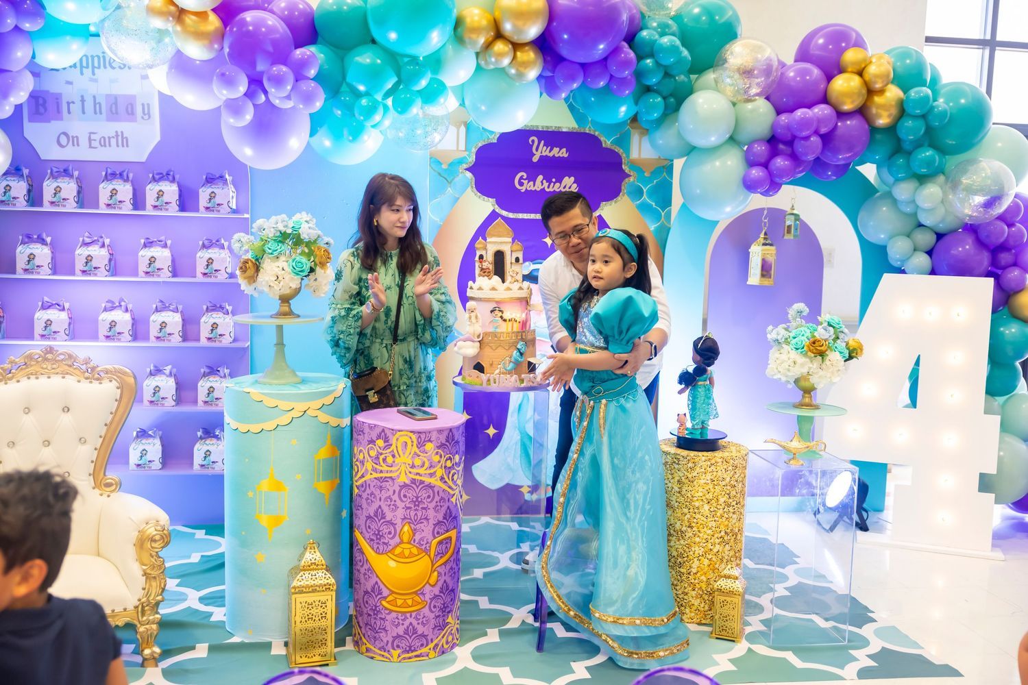 Young girl dressed as Princess Jasmine poses with cake at an Aladdin themed 4th birthday party celebration.