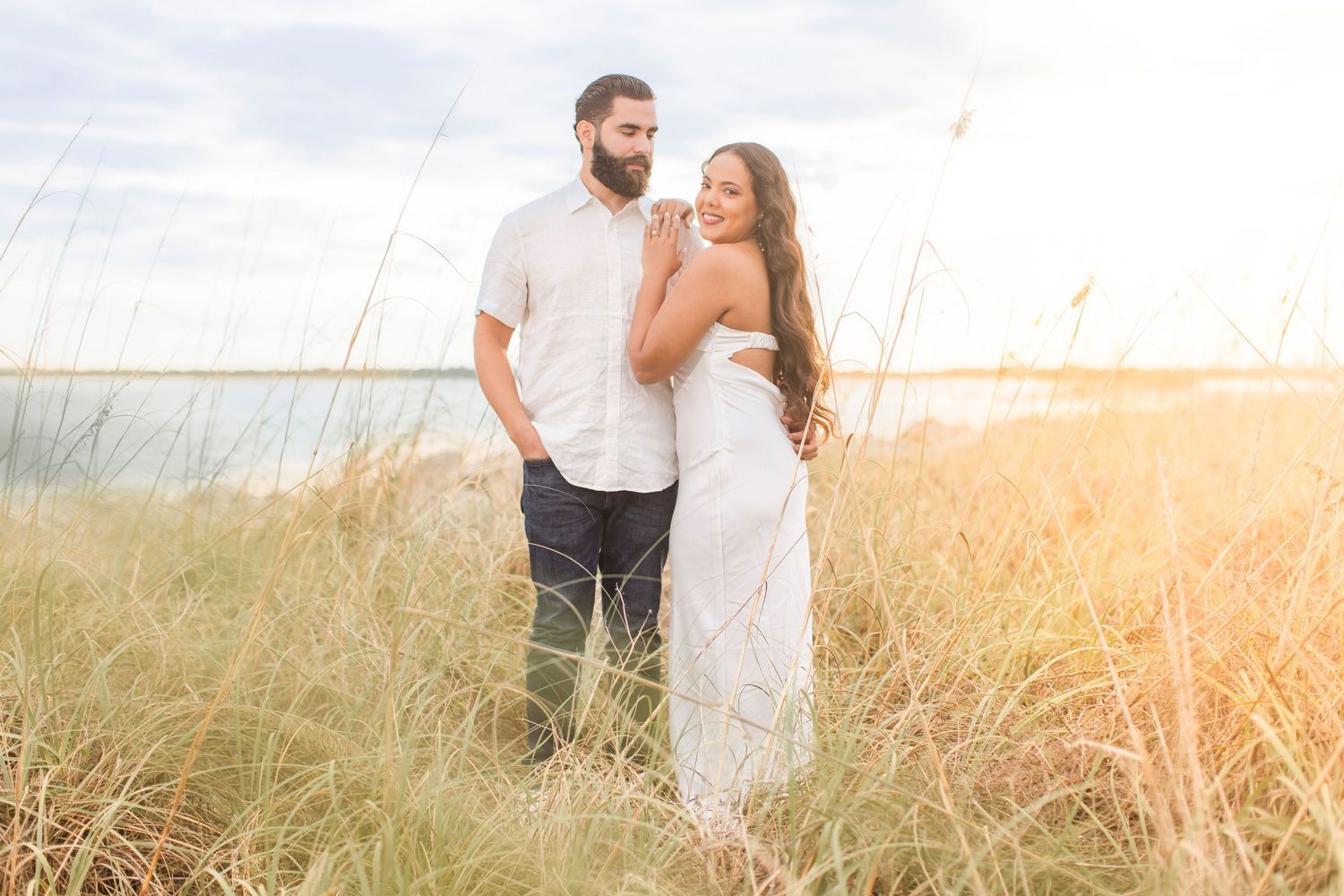 Romantic couple standing in golden beach grass at sunset together.