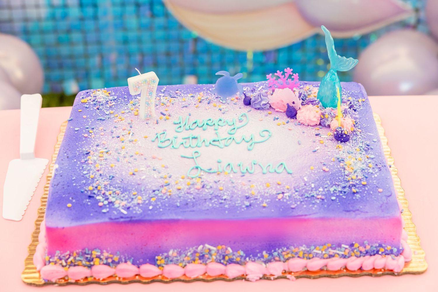 Purple and pink mermaid-themed birthday cake with Happy Birthday inscription and decorative topper.