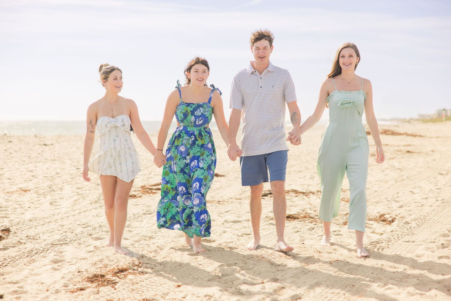 Family of four holding hands and walking together along a sunny sandy beach.