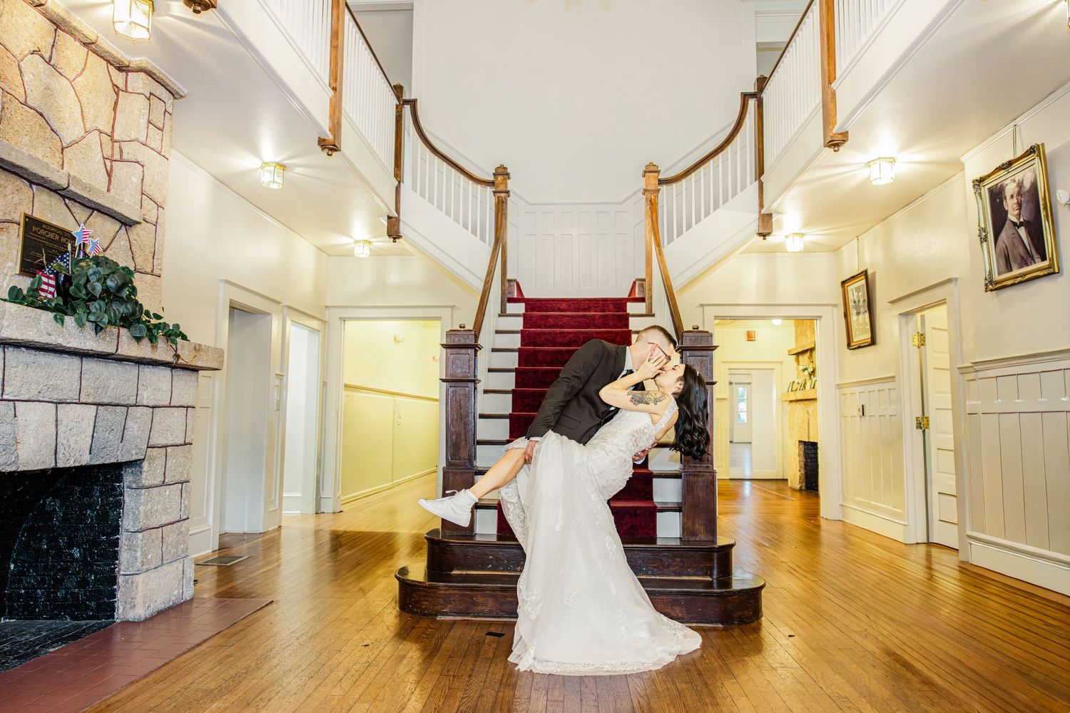 Groom dipping bride near grand staircase with red carpet inside elegant historic wedding venue.
