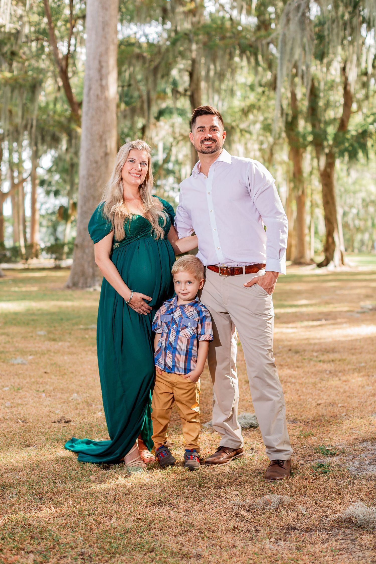 Family maternity portrait with pregnant woman, partner, and young son outdoors.