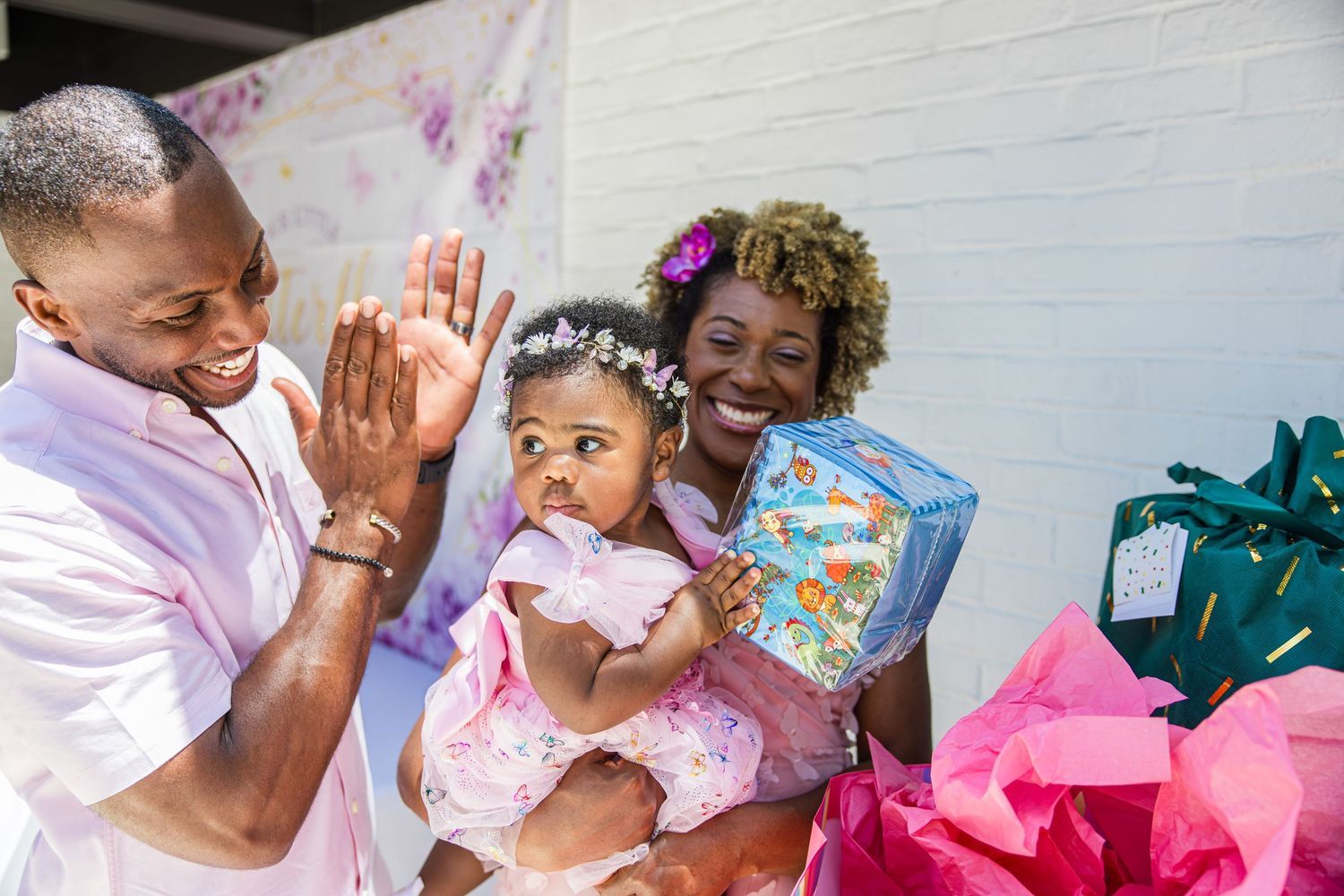 Parents celebrating baby girl's first birthday with gifts and decorations.