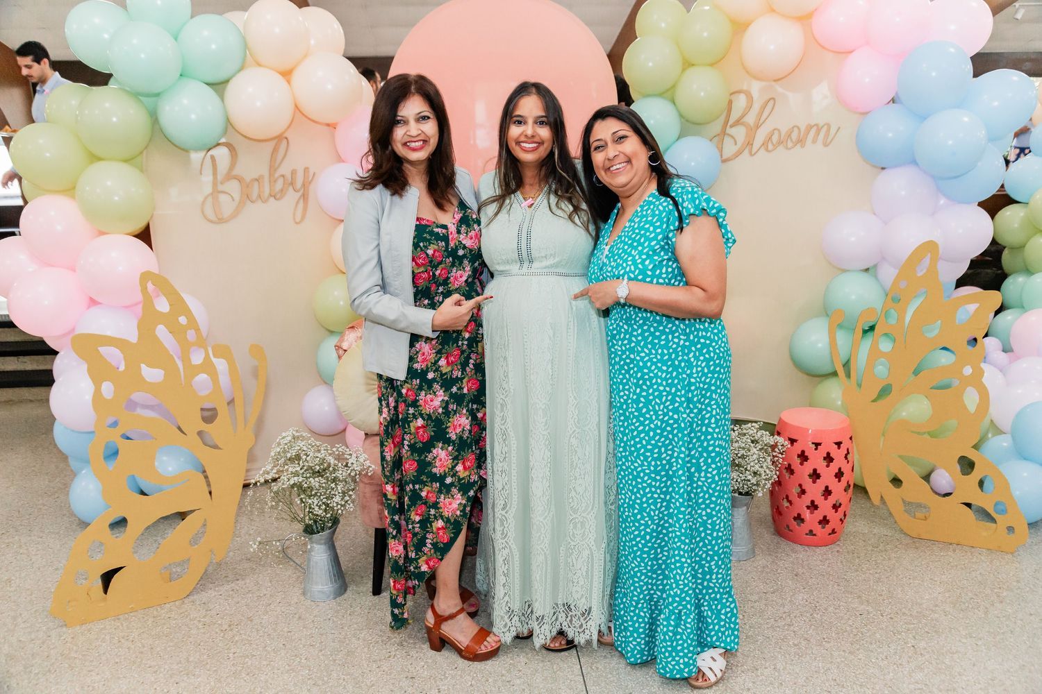 Three women pose together at a Baby in Bloom baby shower with pastel balloon backdrop.