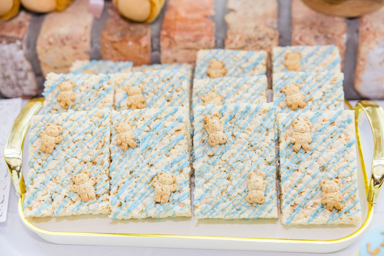 Blue and white rice crispy treats topped with small teddy bear candies arranged on a gold-trimmed serving tray.