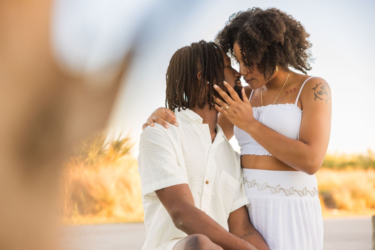 Romantic couple in white outfits sharing an intimate moment outdoors in golden sunlight.
