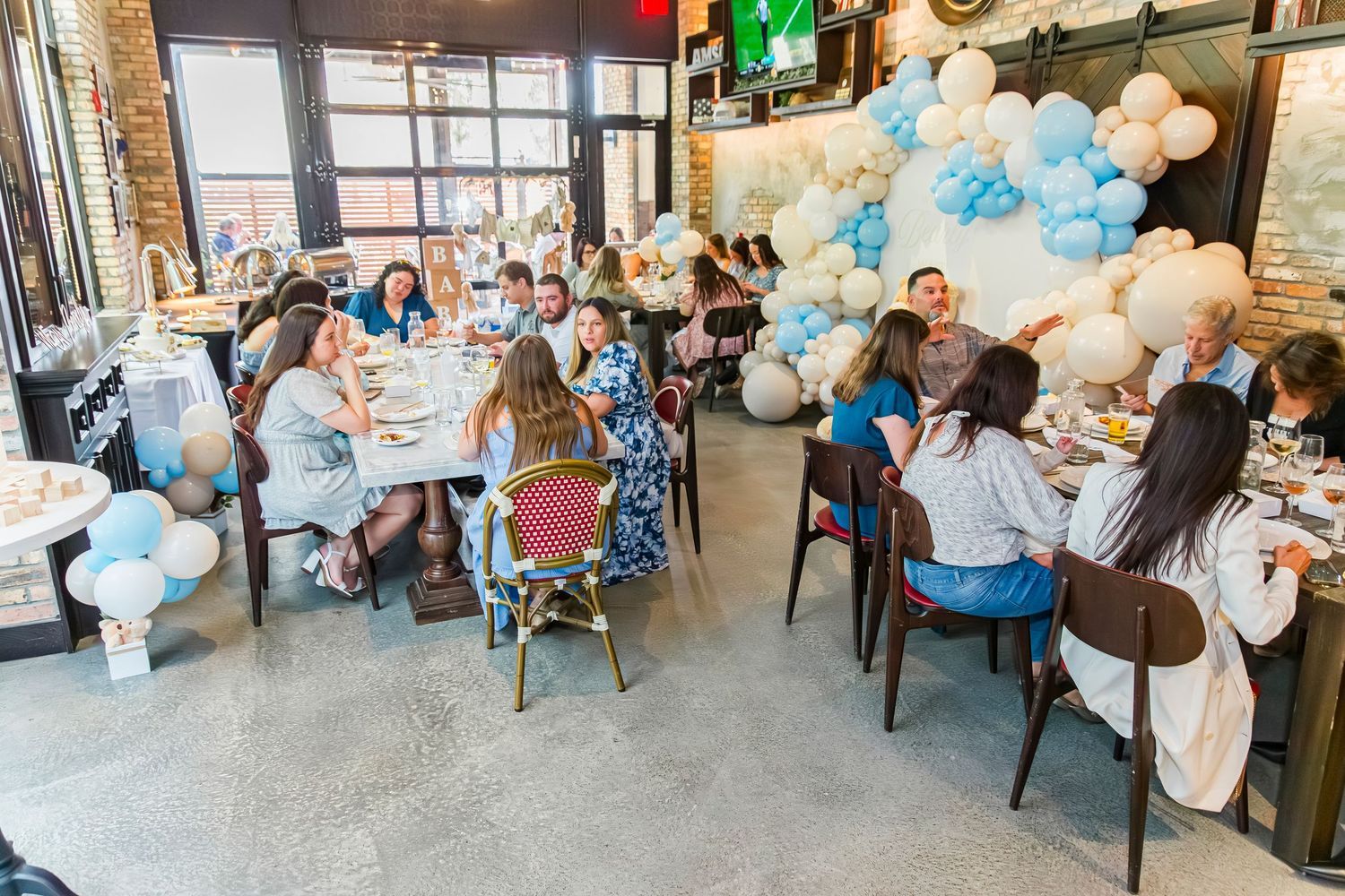 Guests celebrating at a blue and white balloon-decorated baby shower party in a restaurant.