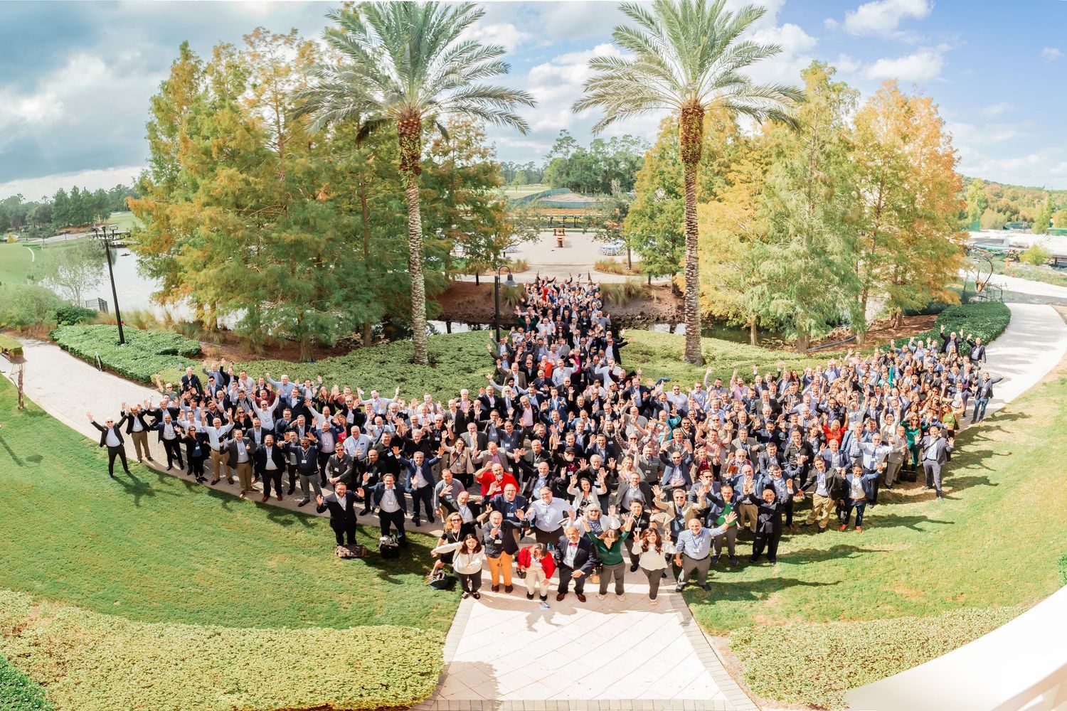Large group of people gathered outdoors for an aerial photo surrounded by palm trees and greenery.