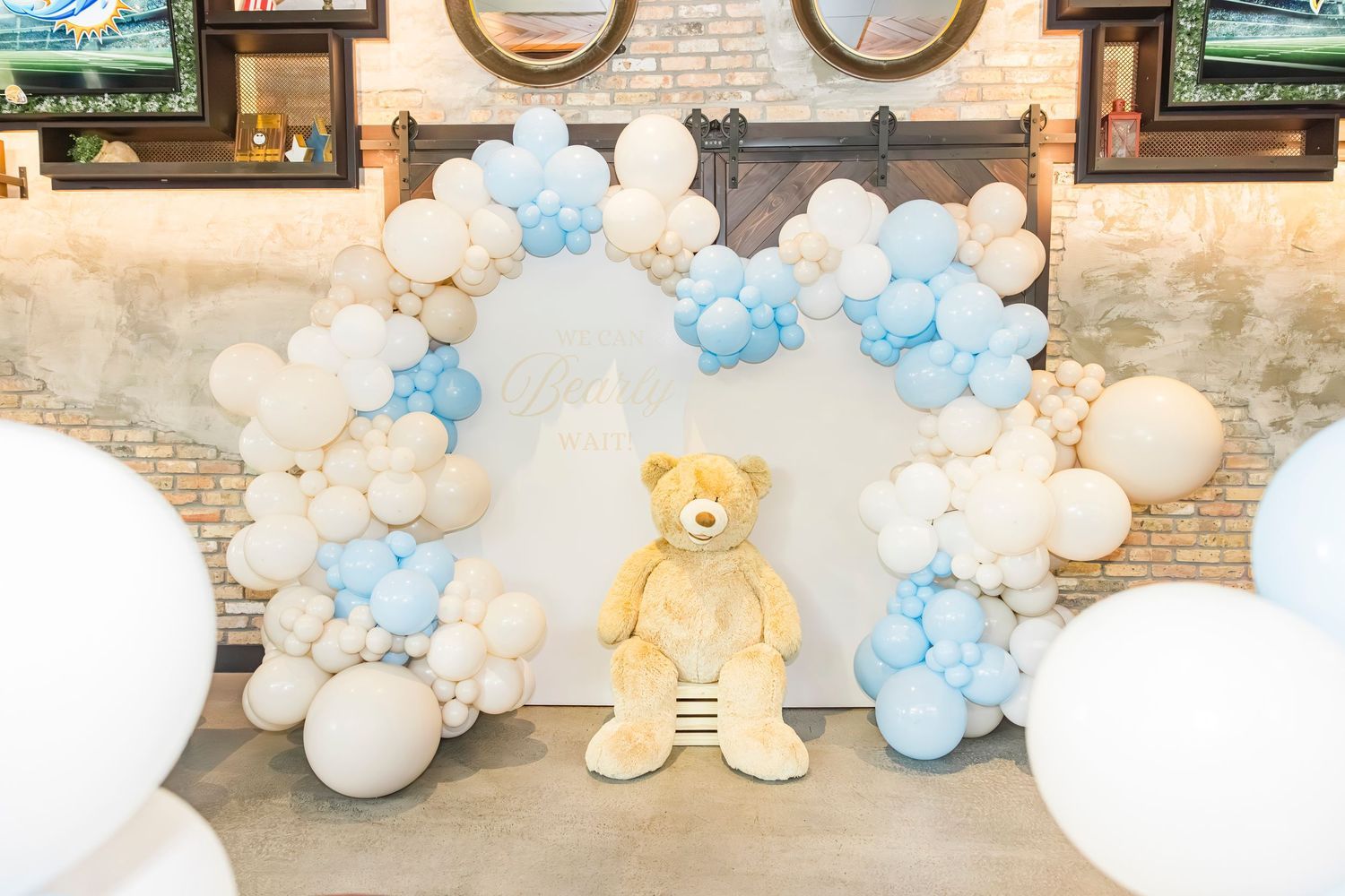 Blue and white balloon arch with giant teddy bear centerpiece for baby shower decoration.