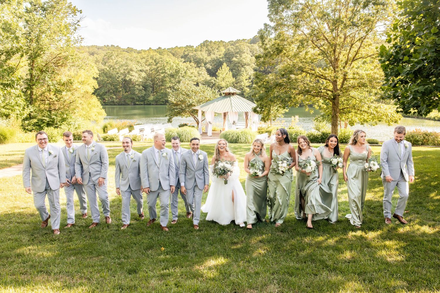 Wedding party walks together on green lawn in coordinating sage and gray attire.