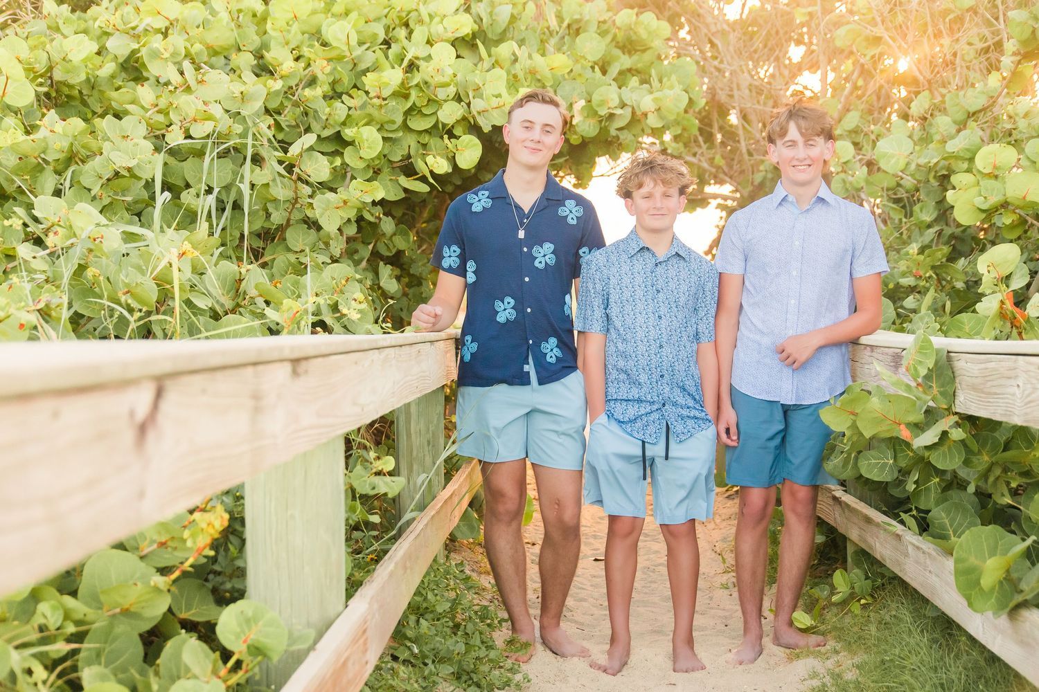 Three teenage boys in matching teal shorts posing on a wooden bridge surrounded by tropical greenery.