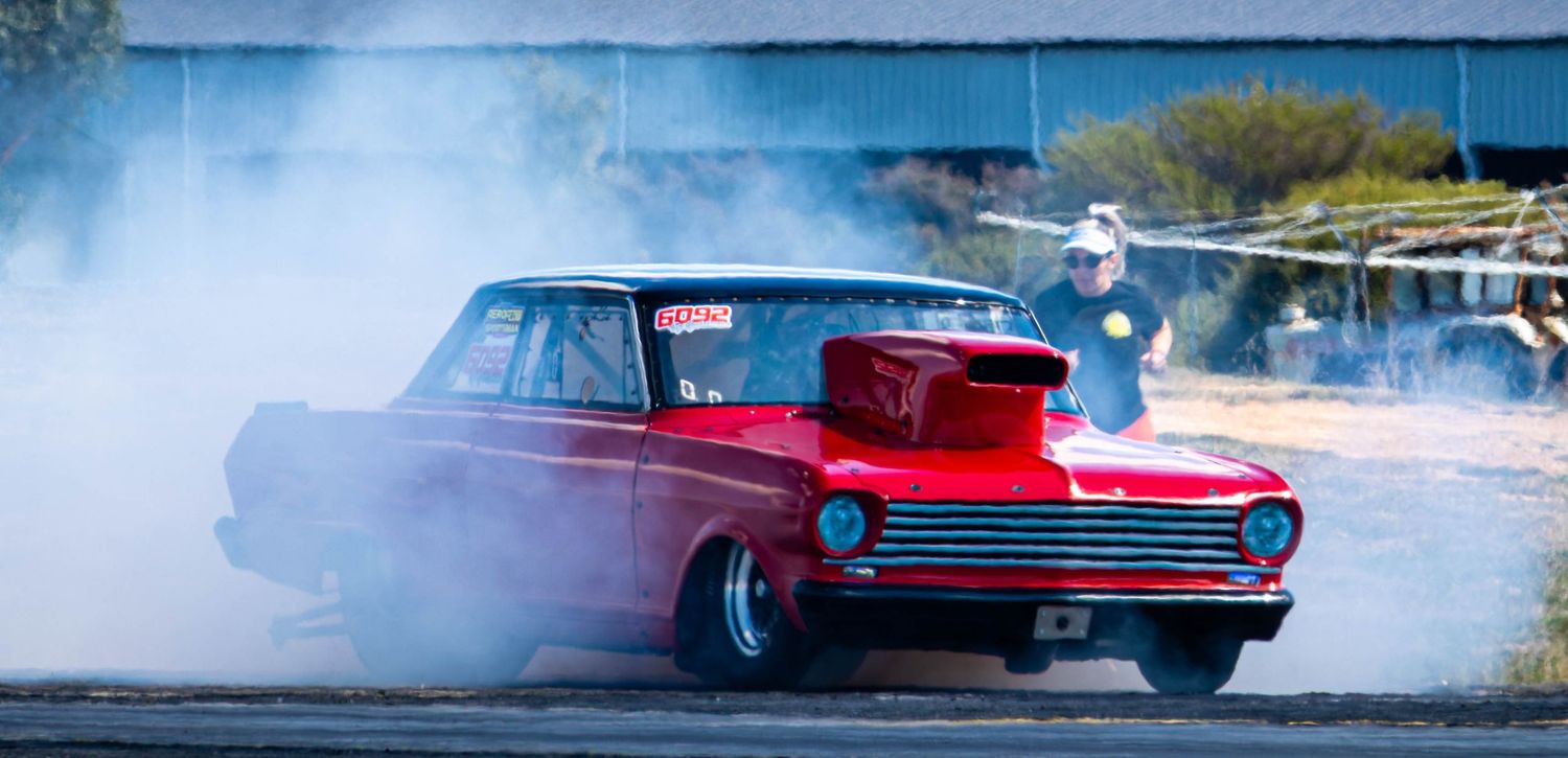 Burnout action shot with red car surrounded by tyre smoke at drag strip