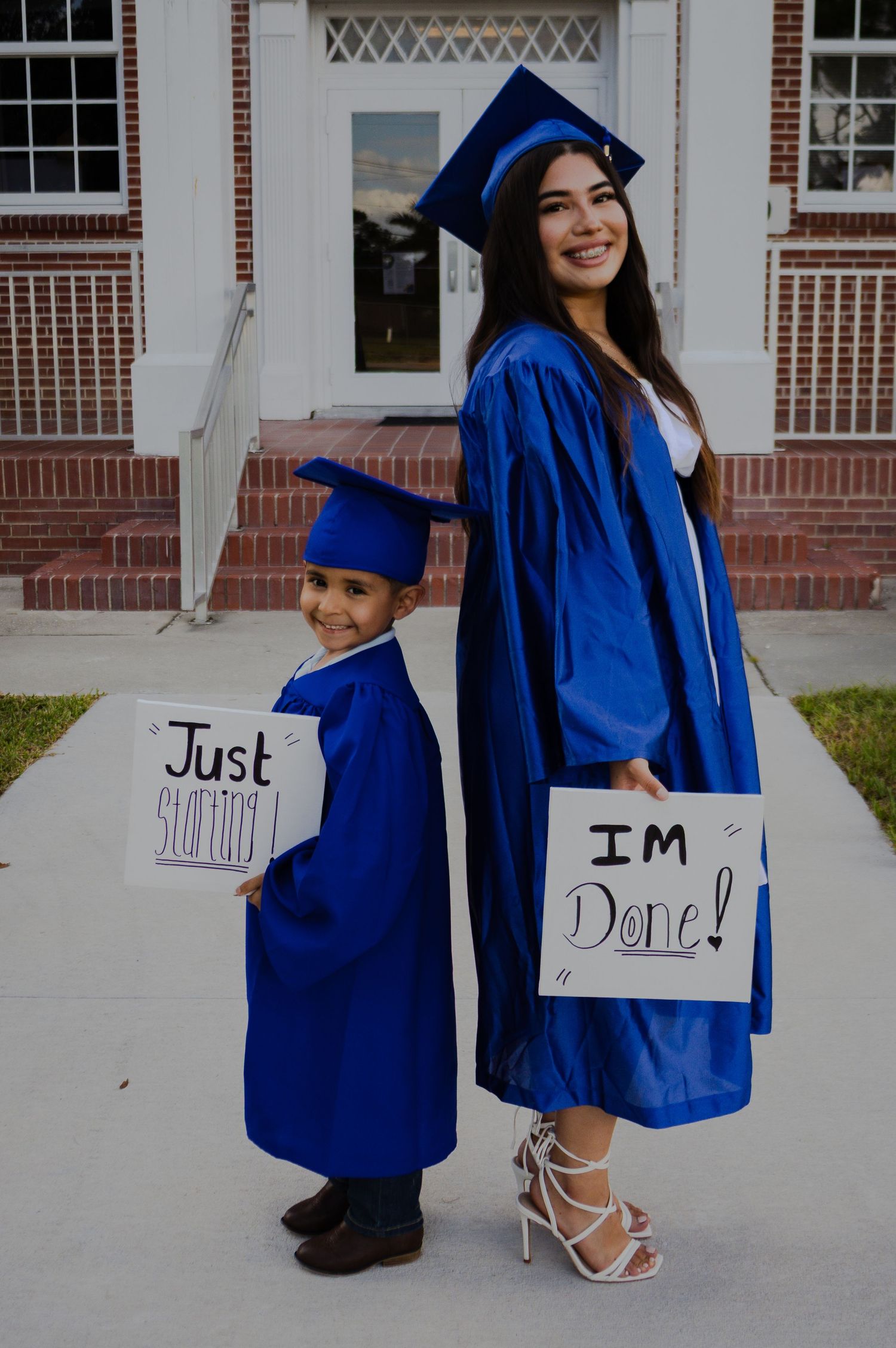 A young woman and child in matching blue graduation caps and gowns hold signs reading I'm Done and Just Starting.