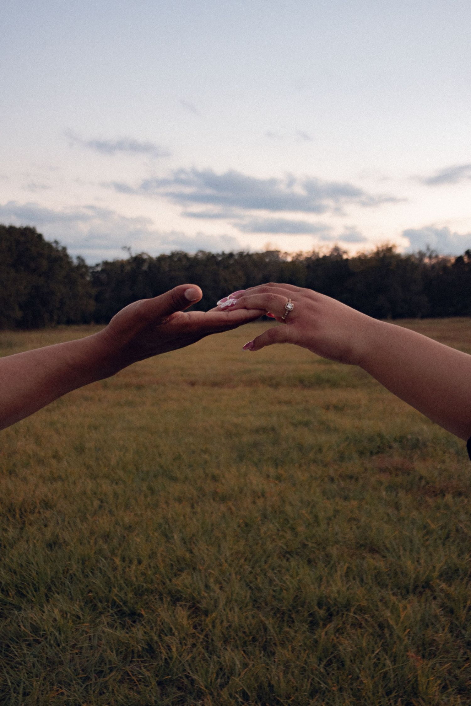 Two hands gently touching fingertips in an open green field at dusk.