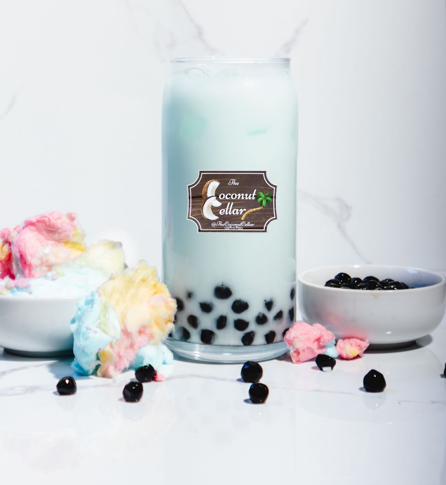 Coconut Cellar bubble tea with black tapioca pearls, cotton candy, and a light blue milk tea in a tall glass.