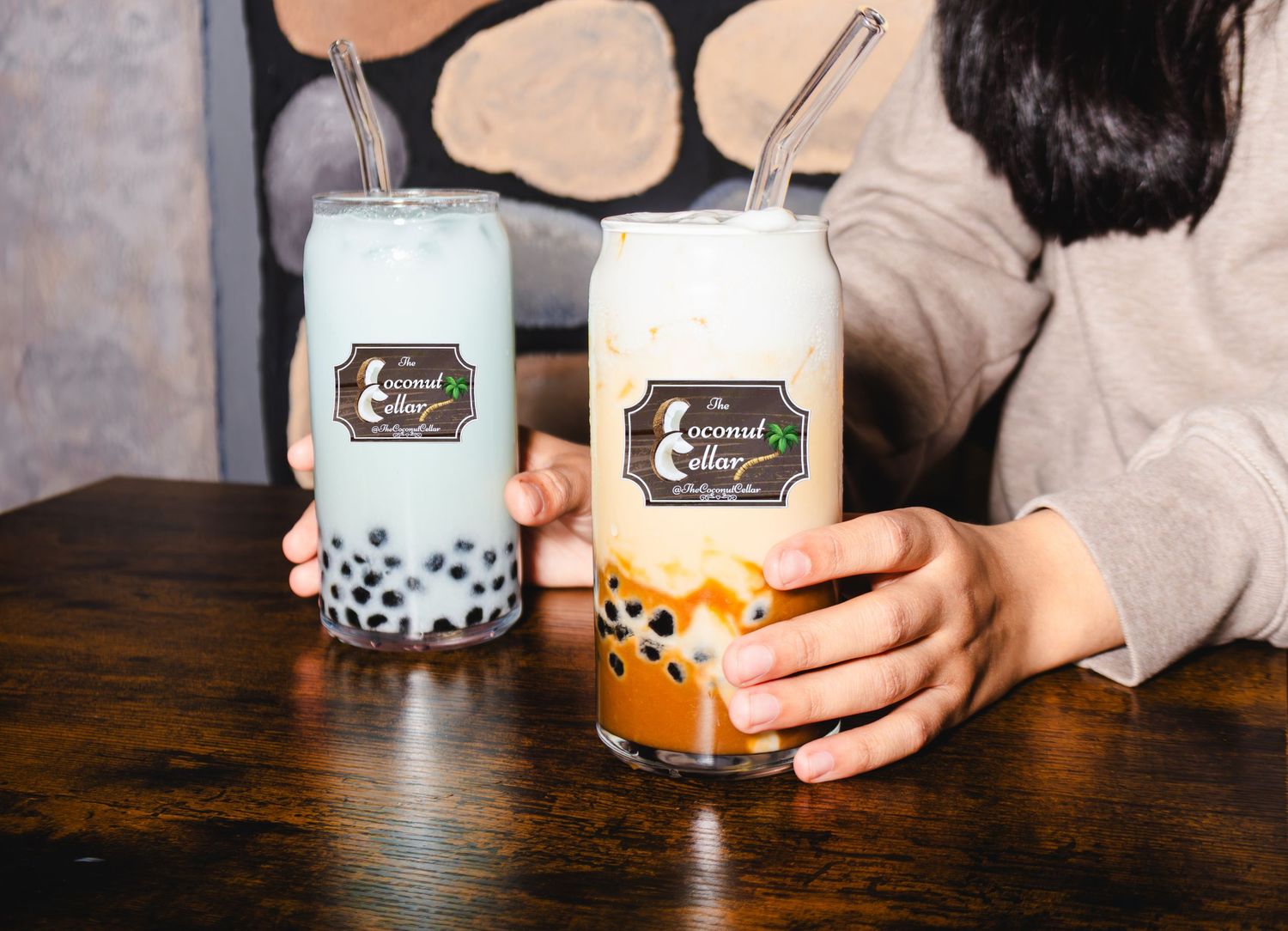 Two coconut milk bubble tea drinks with boba pearls served in glass cups on a wooden table.