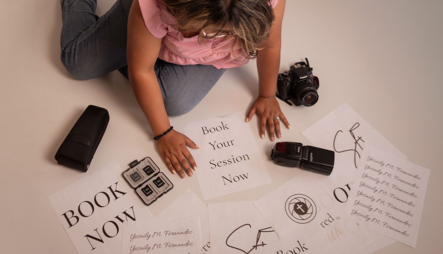 Woman arranging photography booking session promotional papers on floor with cameras nearby.