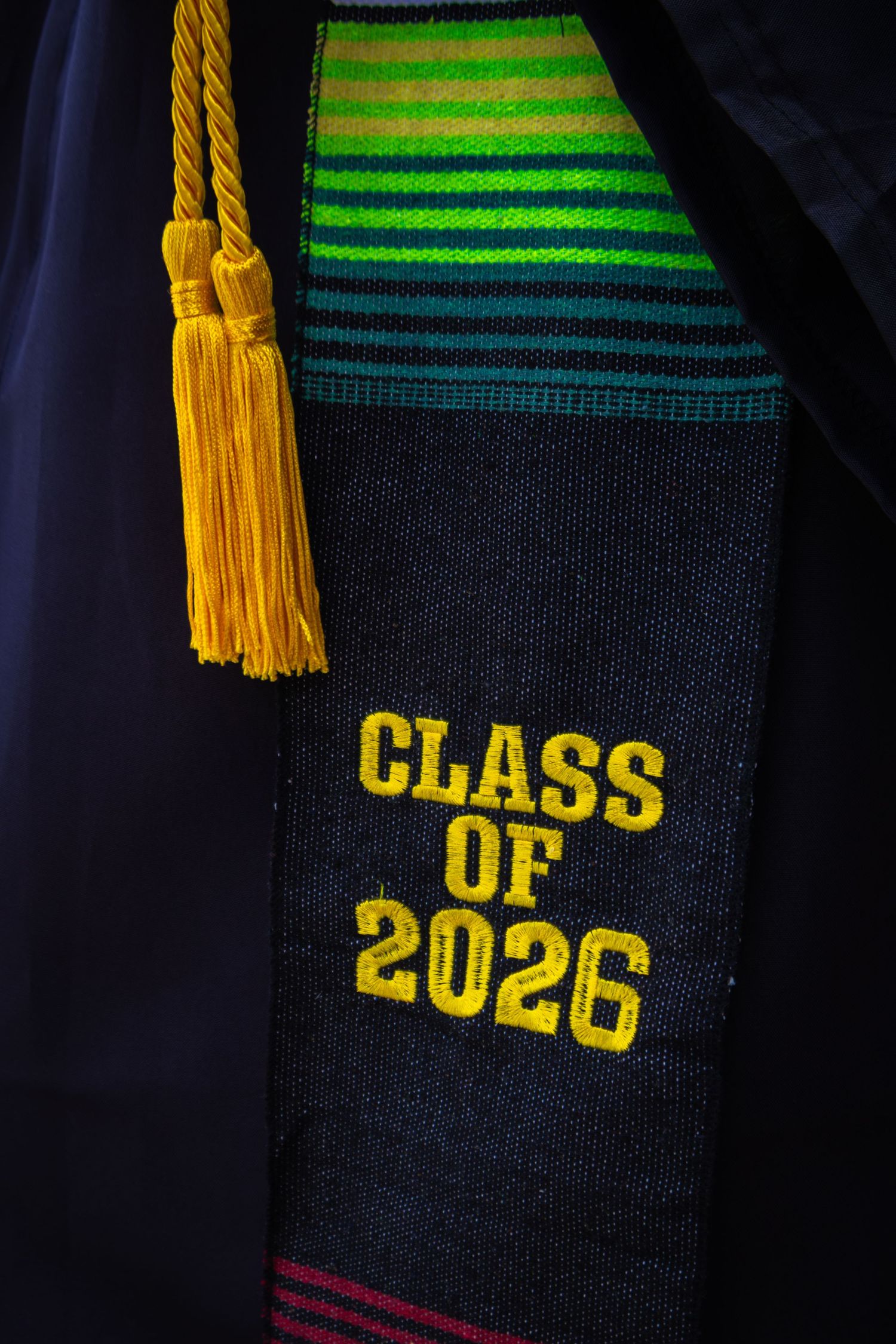 Class of 2026 graduation stole with colorful stripes and yellow tassel on dark academic gown.