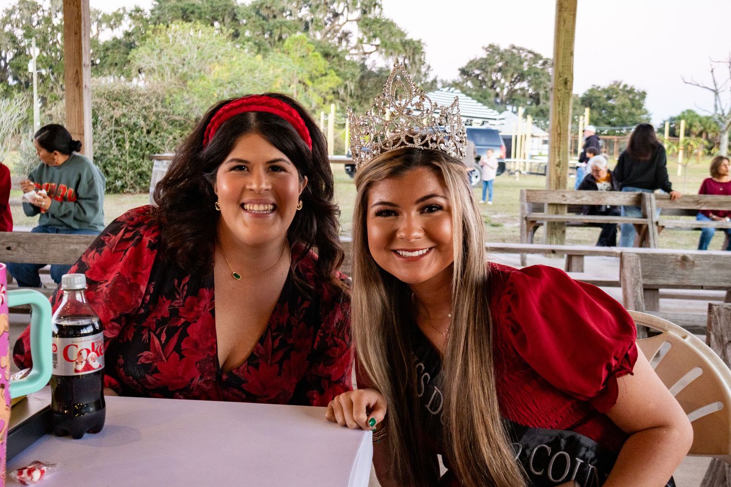 Two smiling women posing together, one wearing a sparkling crown, at an outdoor event.