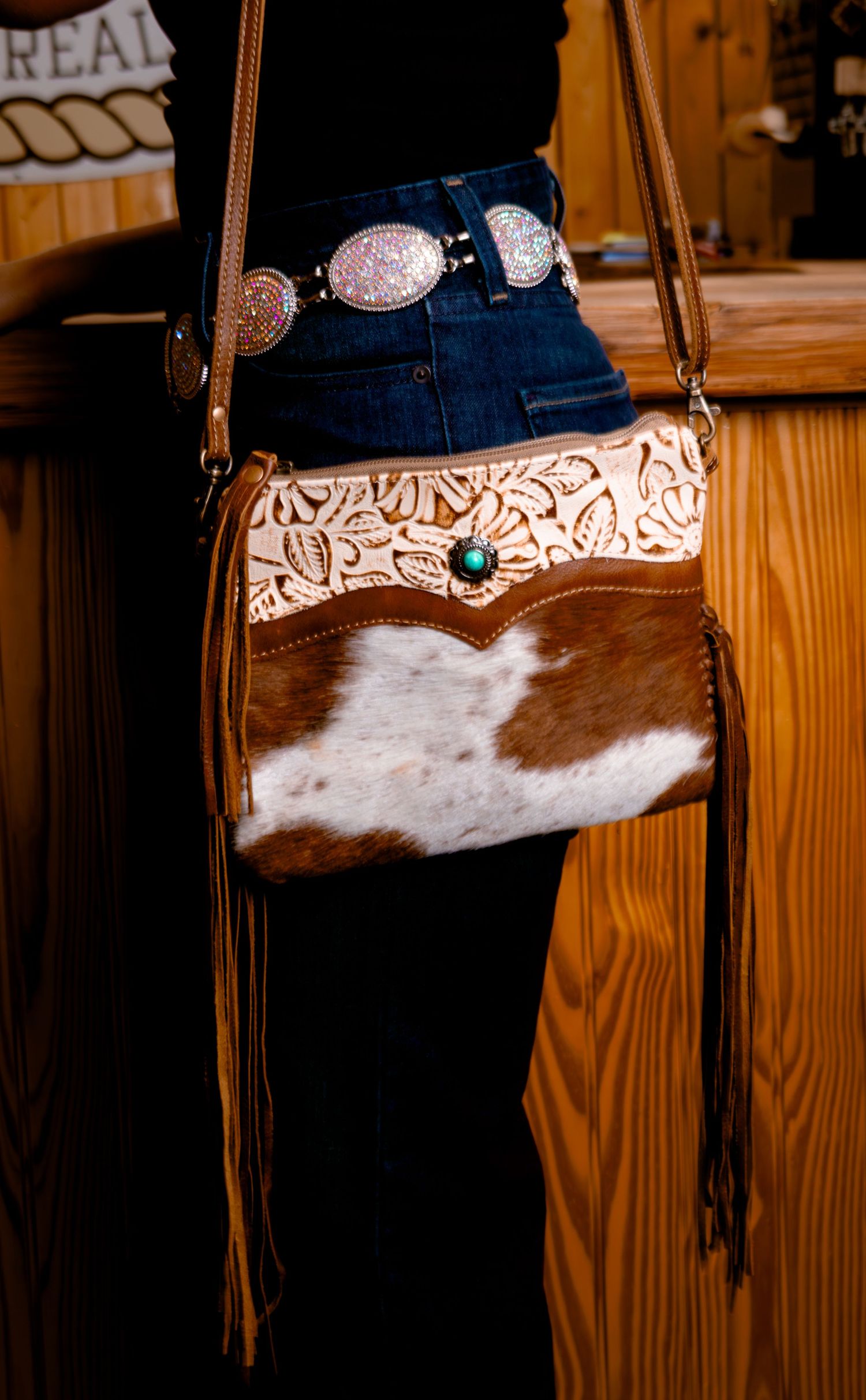 Western leather crossbody bag with tooled floral design, cowhide panel, and turquoise stone accent.