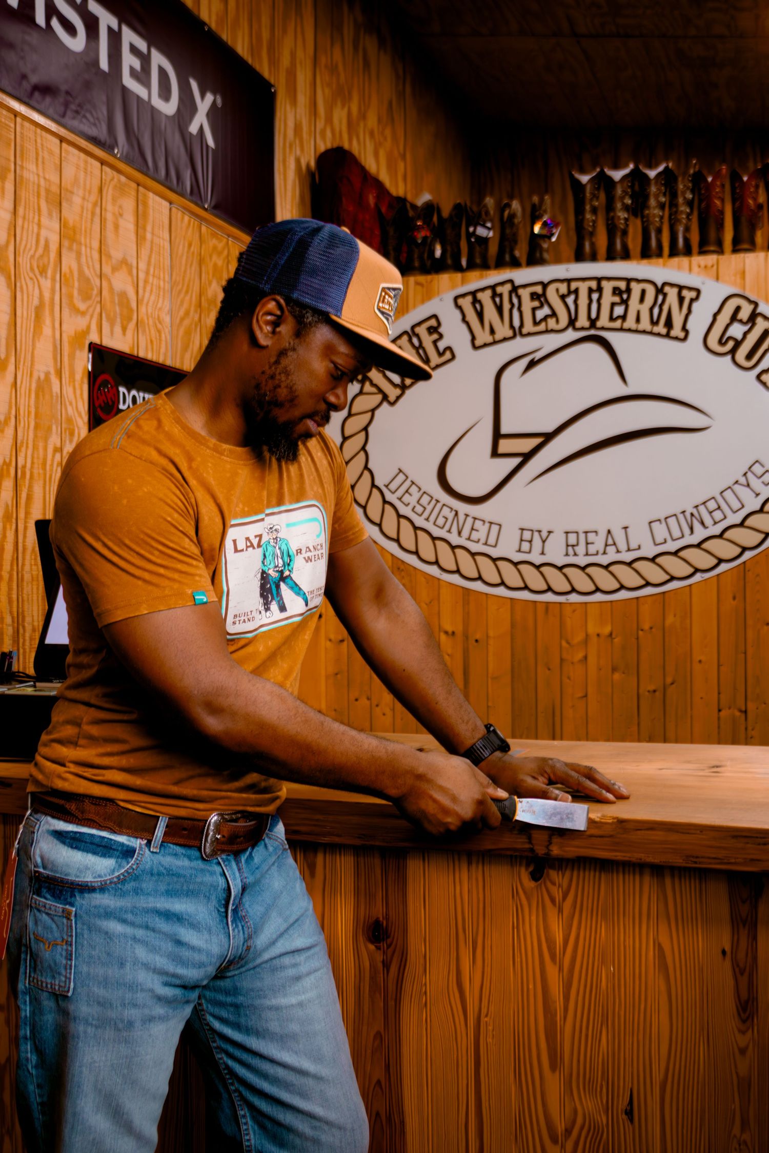 Man in orange graphic tee examining product at counter of The Western Cut western store.