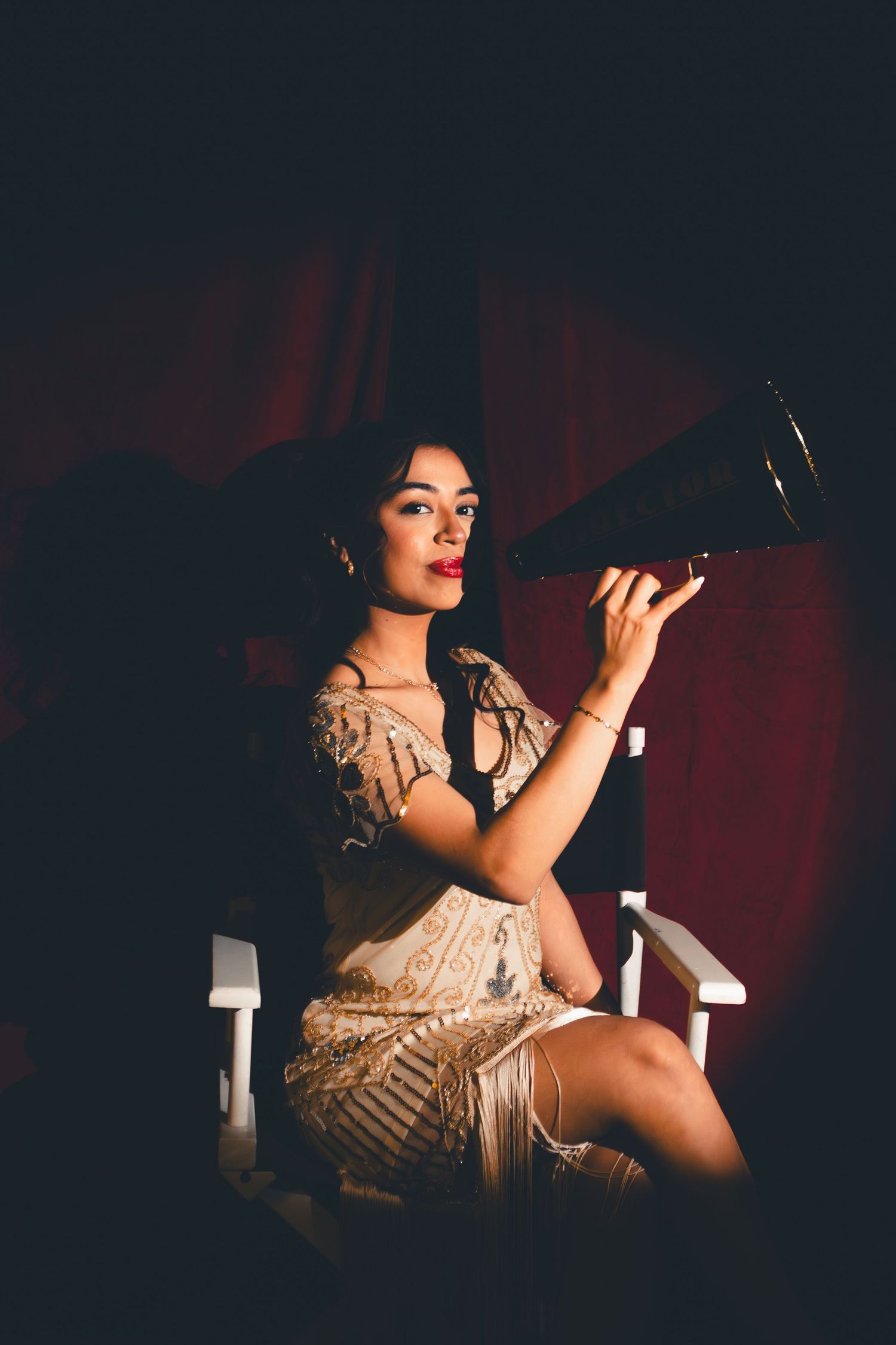 Elegant woman in beige sequin dress holding megaphone in dramatic dark setting.