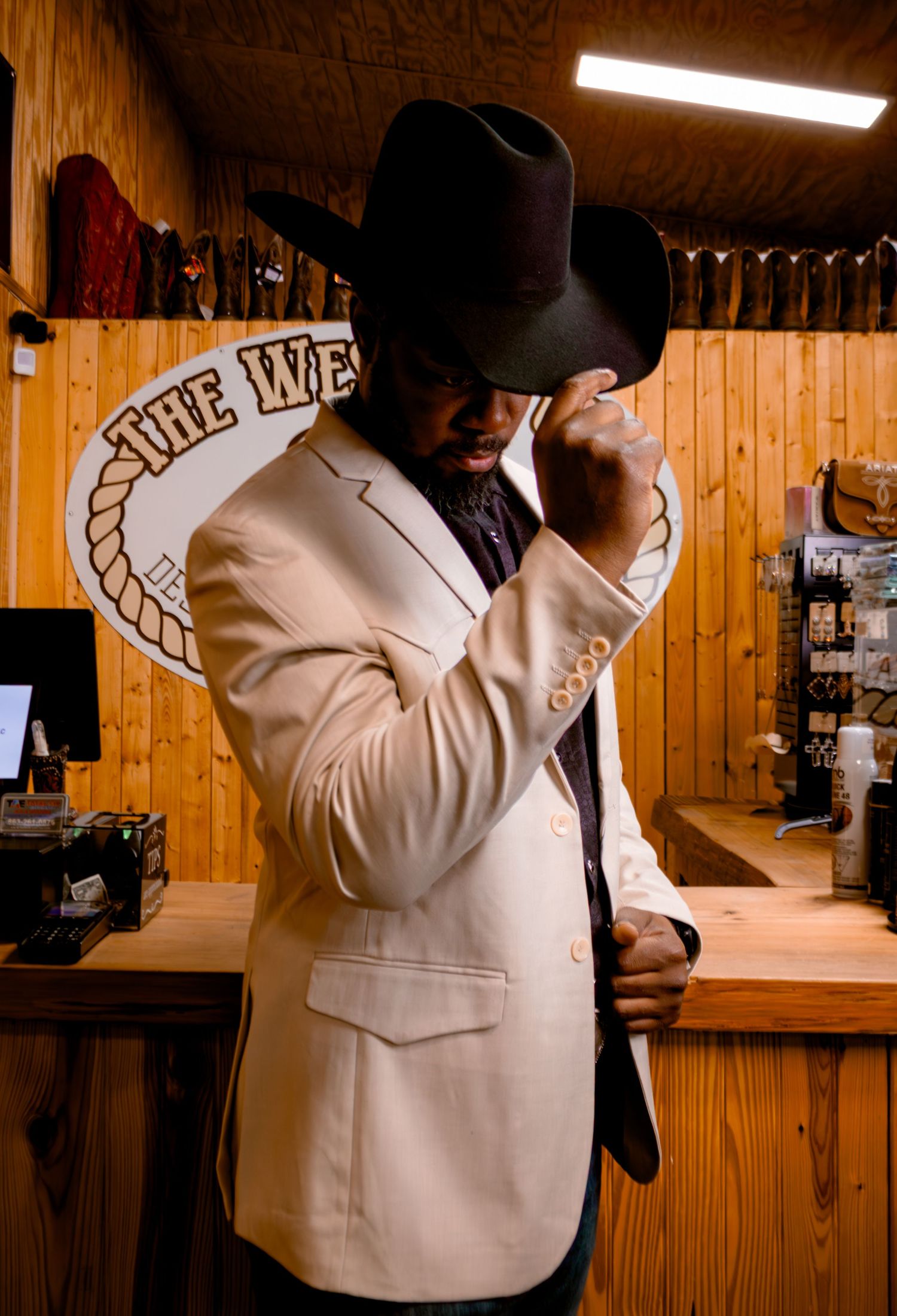 Man in cream blazer and black cowboy hat posing inside The Western Cut western wear store.