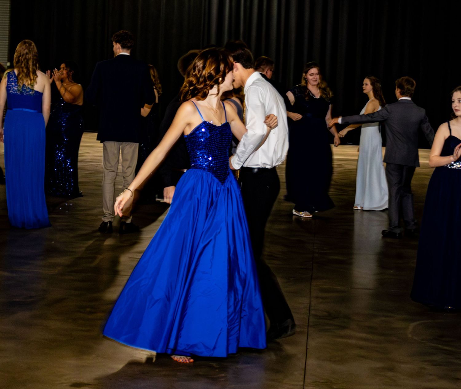 A woman in a royal blue sequined ball gown dances with a partner at a formal evening event.