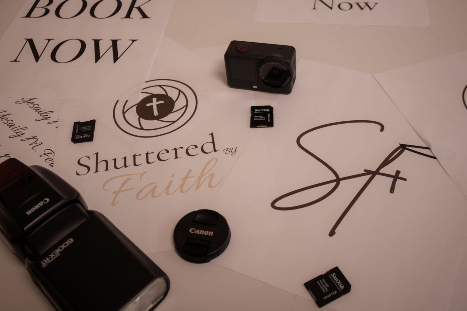 Camera equipment and SD cards arranged on Shuttered by Faith photography branding materials with Book Now text.
