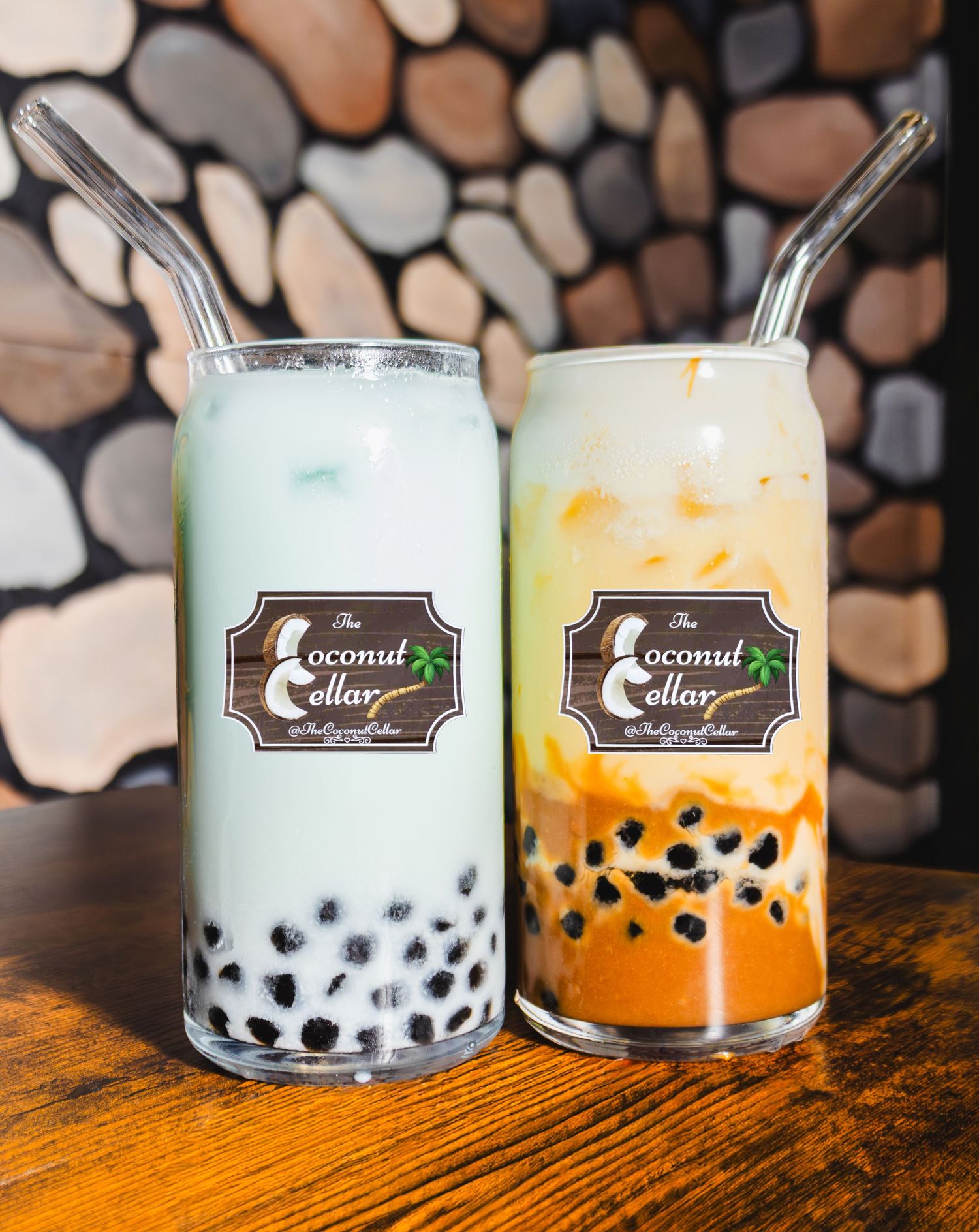Two Coconut Cellar boba drinks, mint green and orange, with black tapioca pearls on wooden table.
