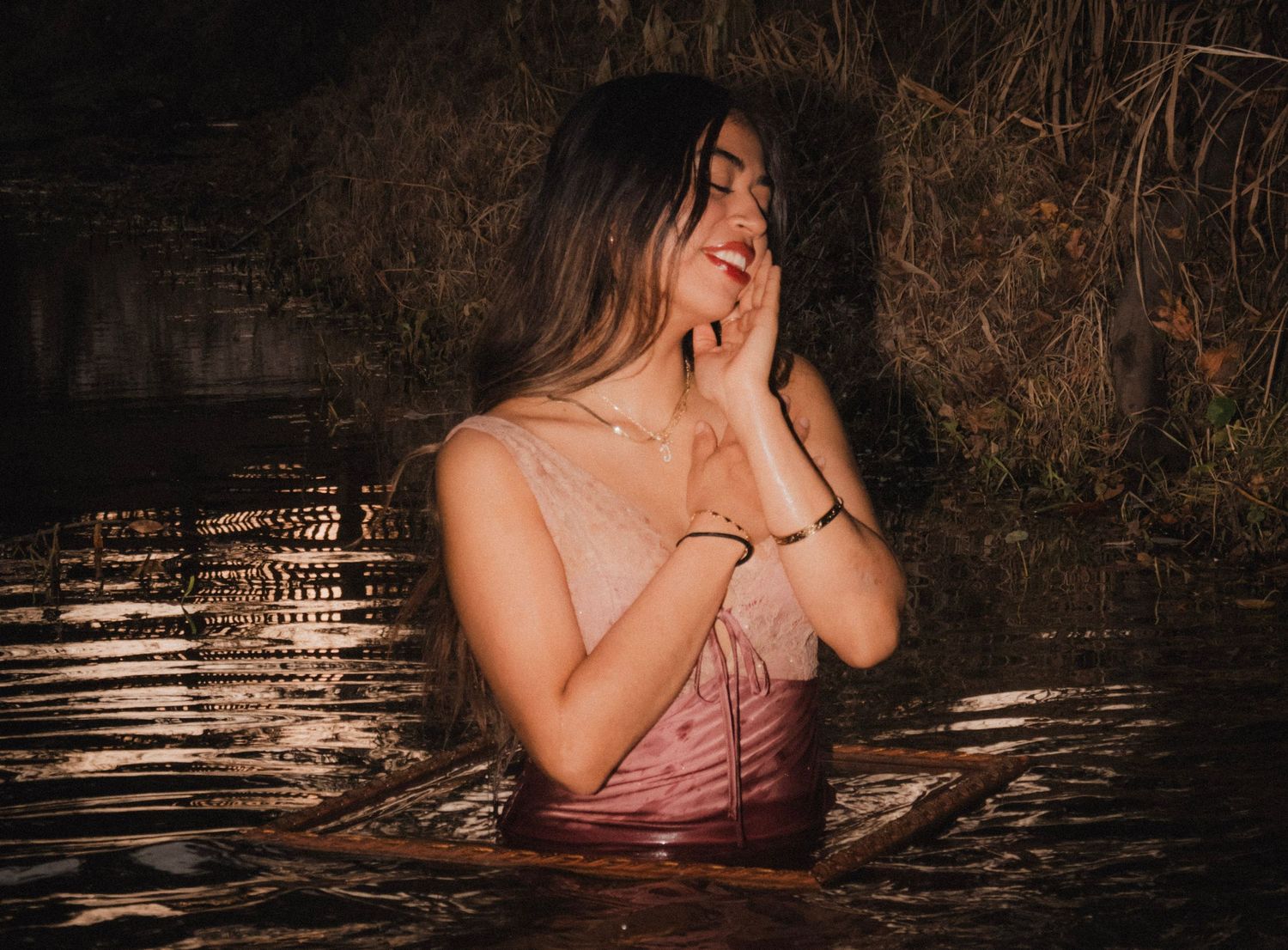 Young woman smiling joyfully while sitting in a natural water pool at night.