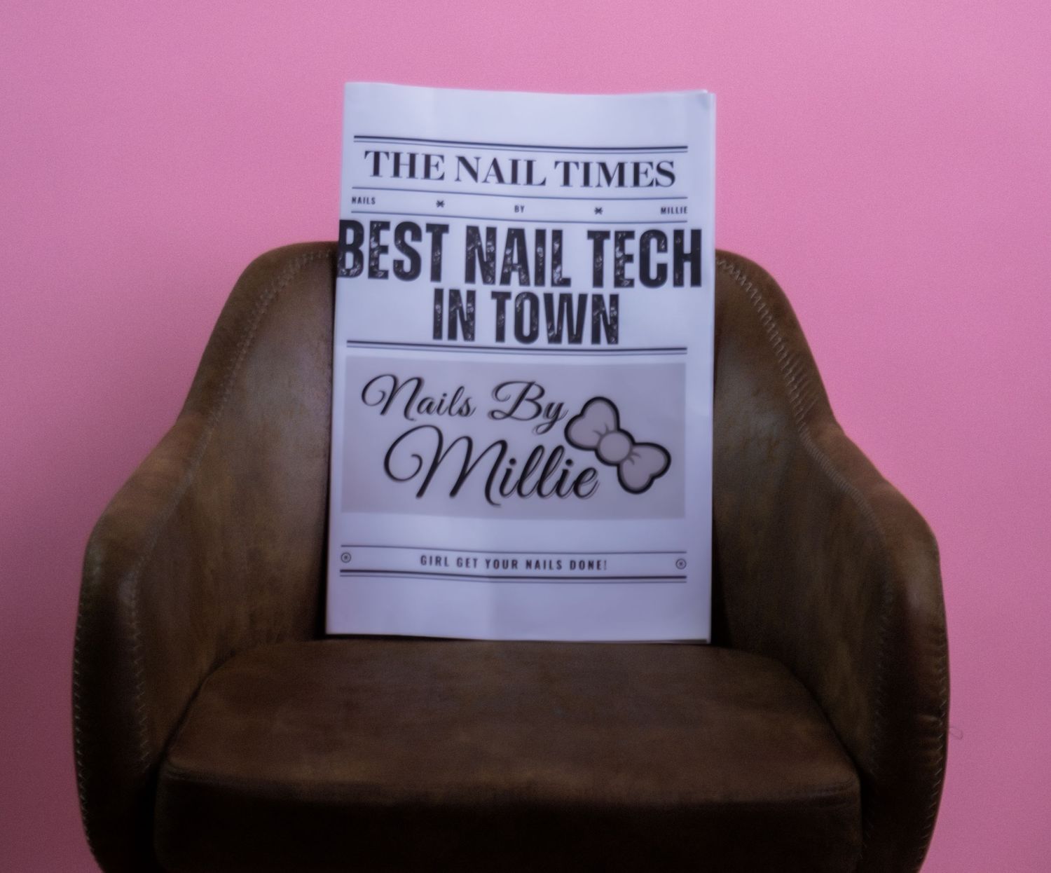 The Nail Times newspaper headline reading Best Nail Tech in Town by Nails By Millie on brown chair.
