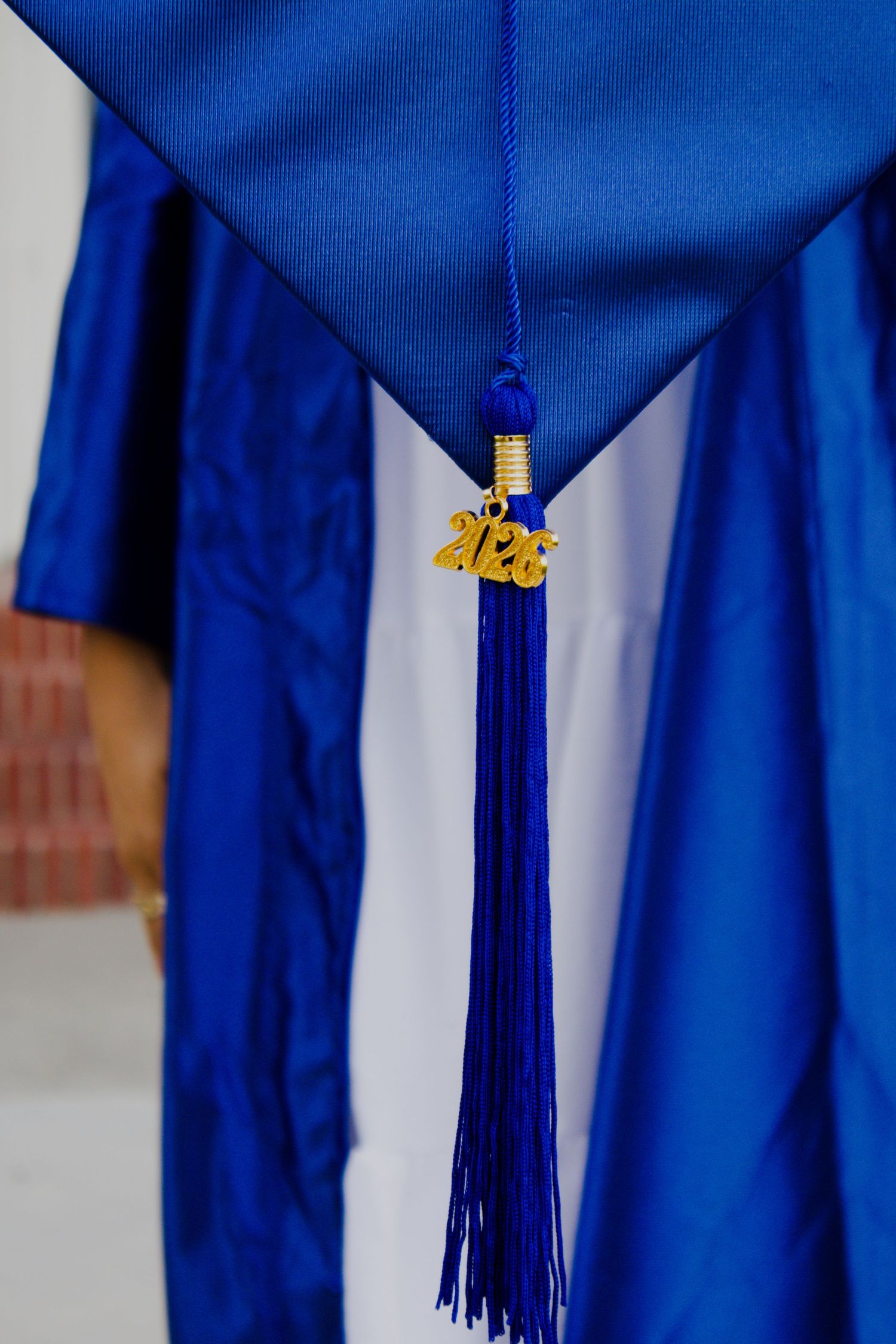 Blue graduation cap and gown with gold 2026 tassel charm, close-up detail shot of academic regalia.
