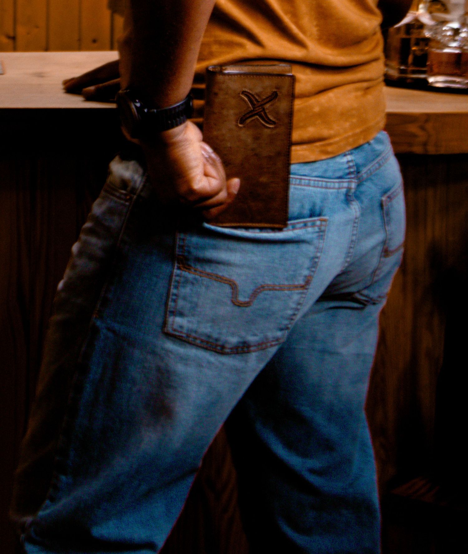 Man holding brown leather bifold wallet with X logo detail at western apparel store.