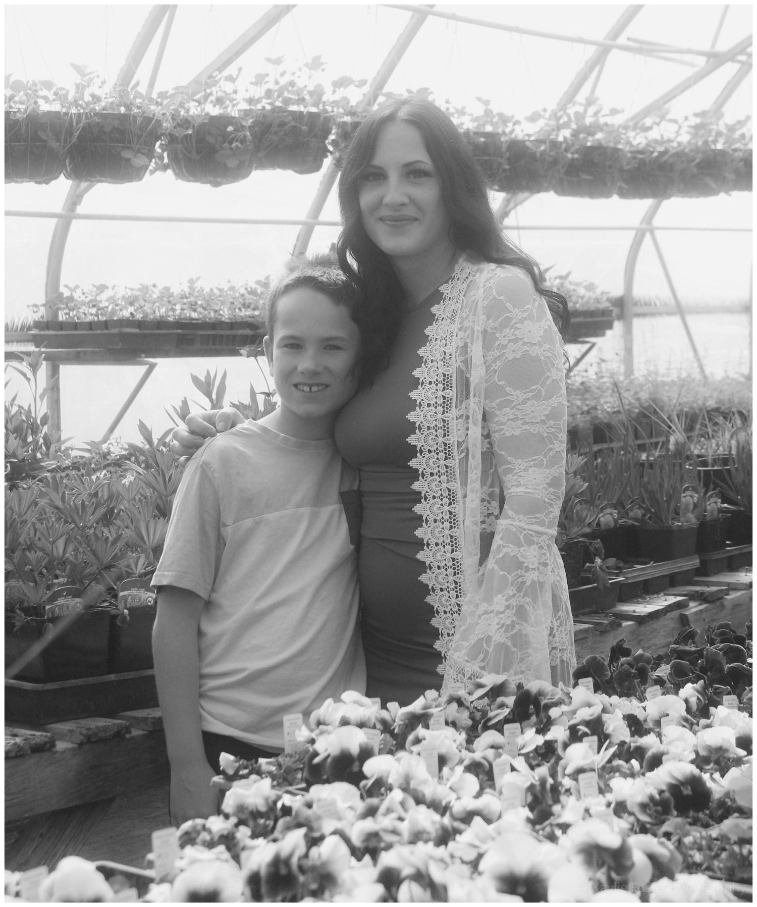 Woman and child smiling together among flowers in a greenhouse.