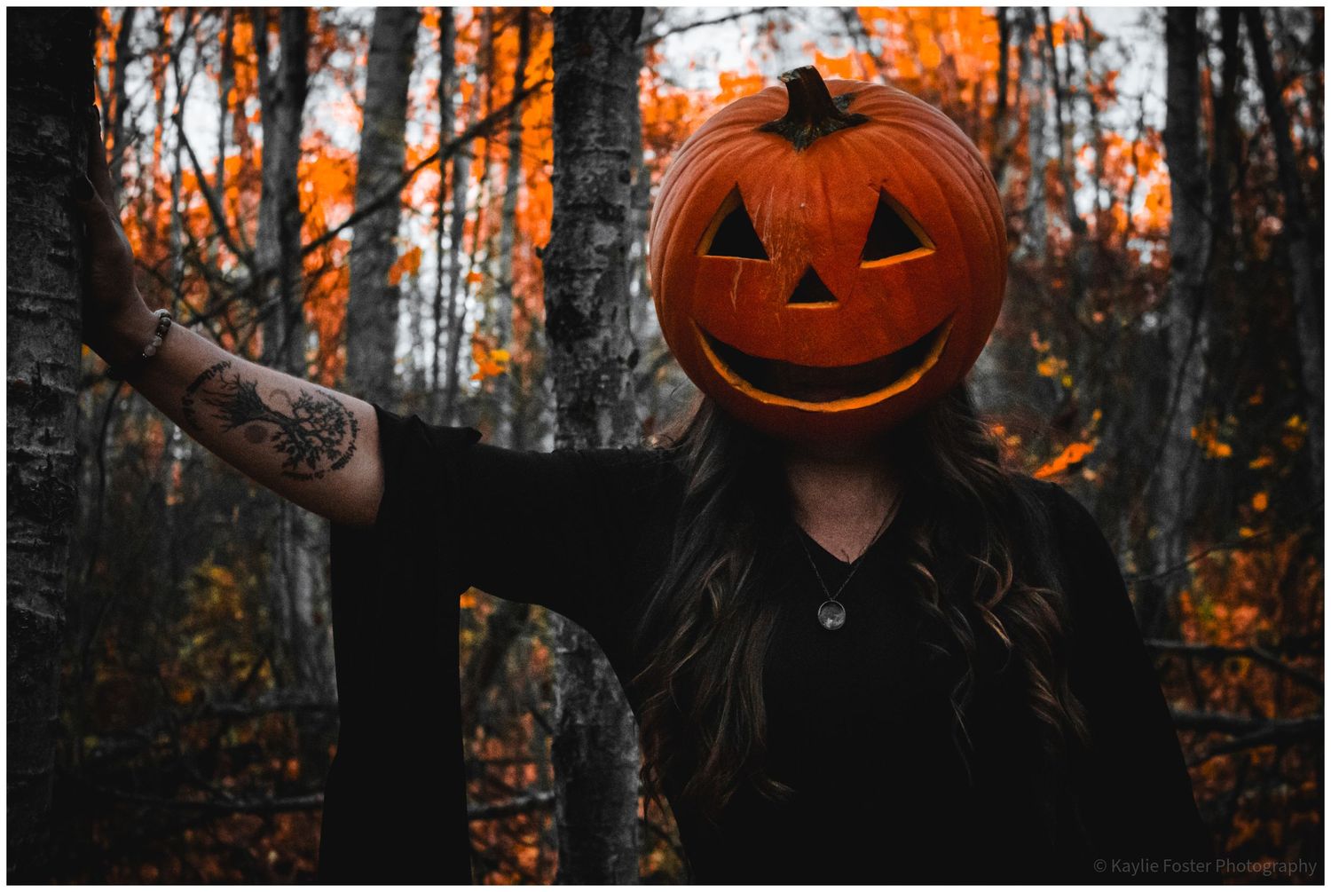 Woman with jack-o-lantern pumpkin head in autumn forest, Halloween costume with tattoo sleeve.