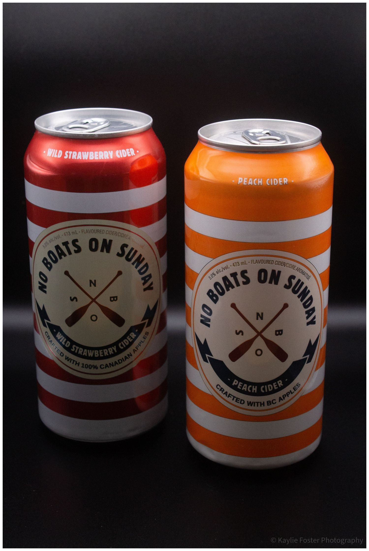 Two No Boats On Sunday cider cans, Wild Strawberry and Peach, in red and orange striped designs on dark background.