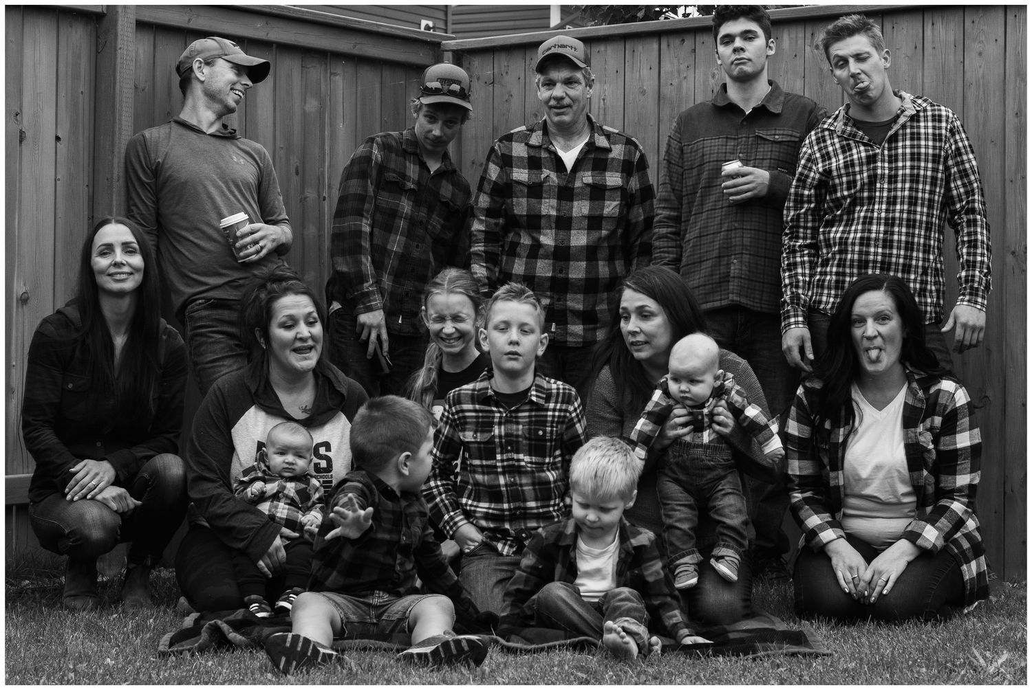 Black and white extended family portrait with adults and children posed in a backyard setting.