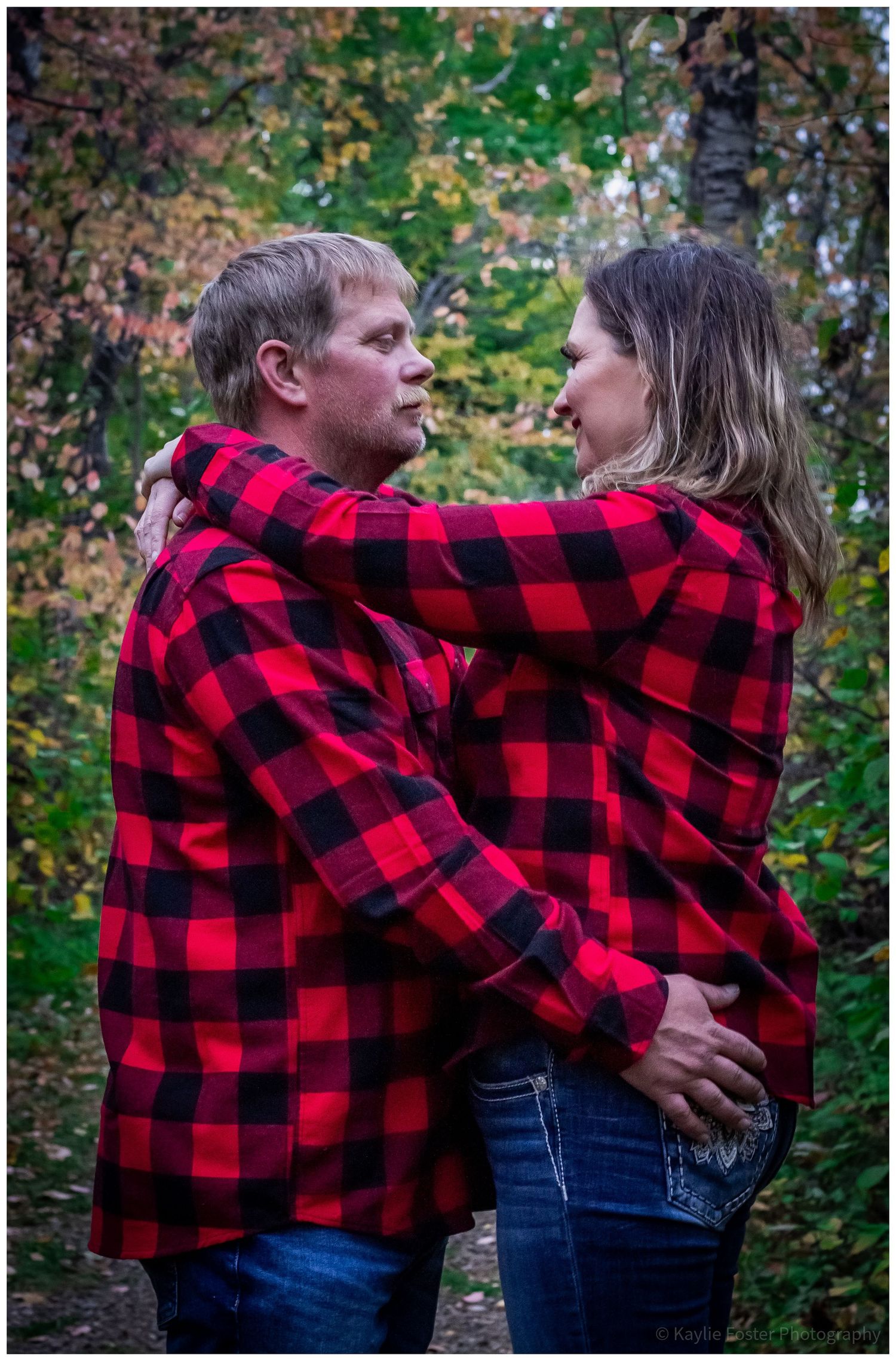 Couple in matching red plaid flannel shirts embracing in an autumn forest setting.