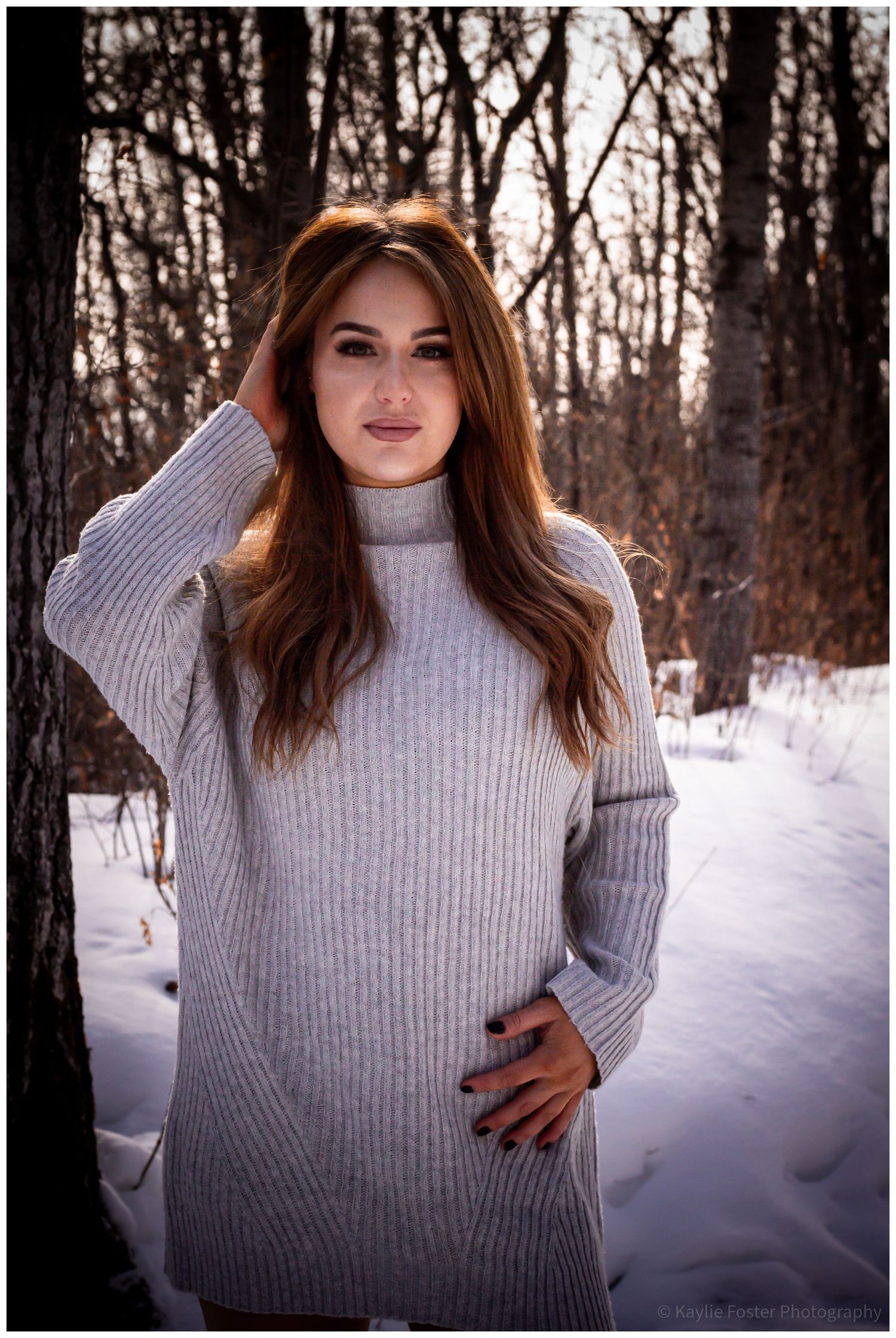 Beautiful young woman in gray turtleneck sweater dress posing in snowy winter forest.