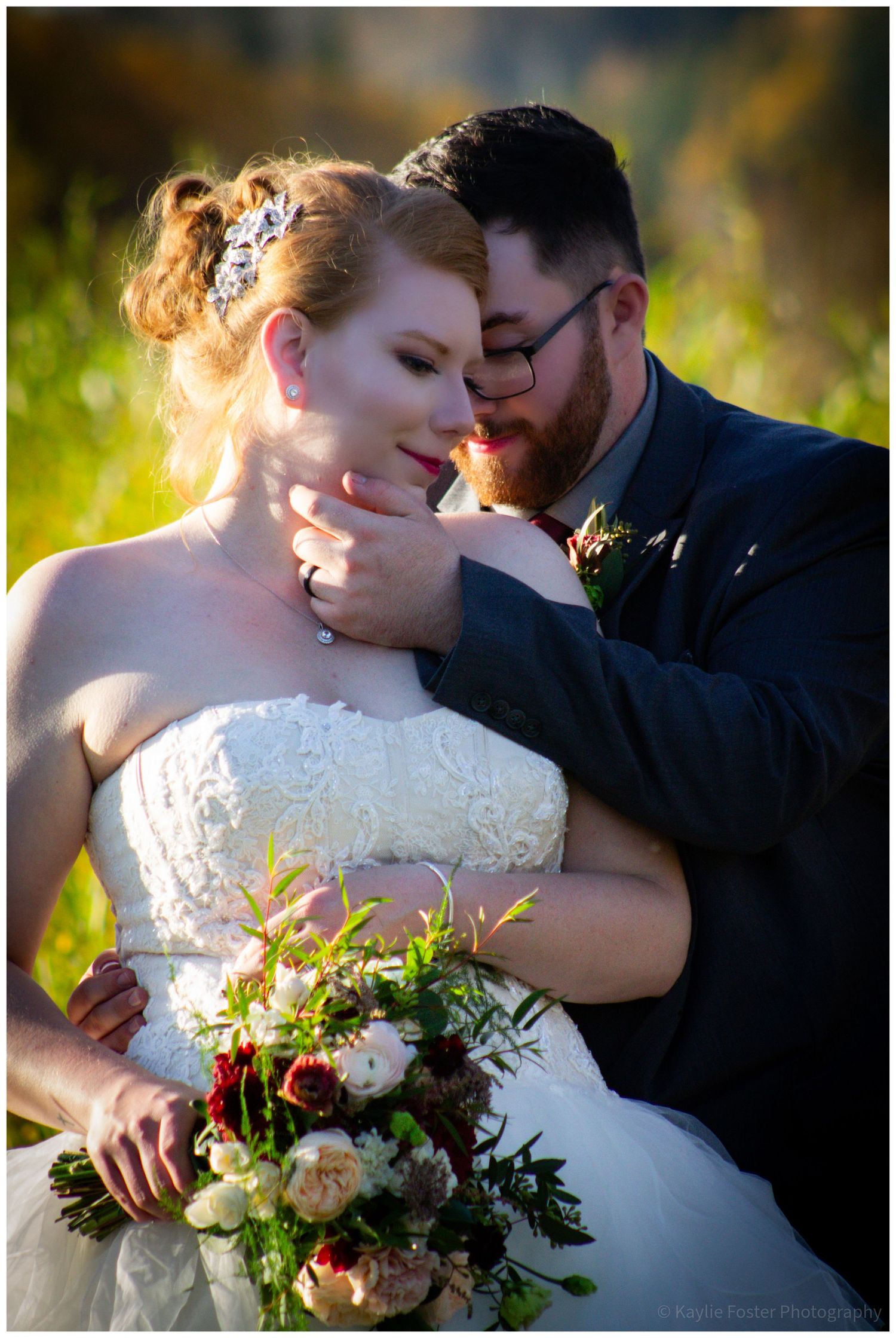 Bride and groom share an intimate moment outdoors, she holds a lush bouquet while he tenderly cradles her face.