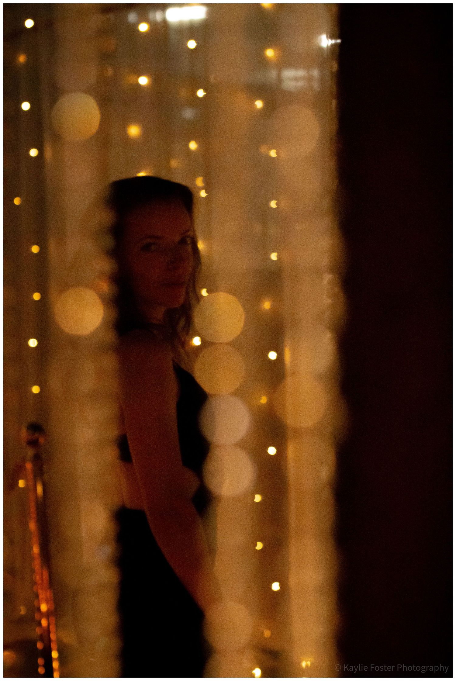 Woman silhouetted against a glowing curtain of warm fairy lights in a dimly lit venue.