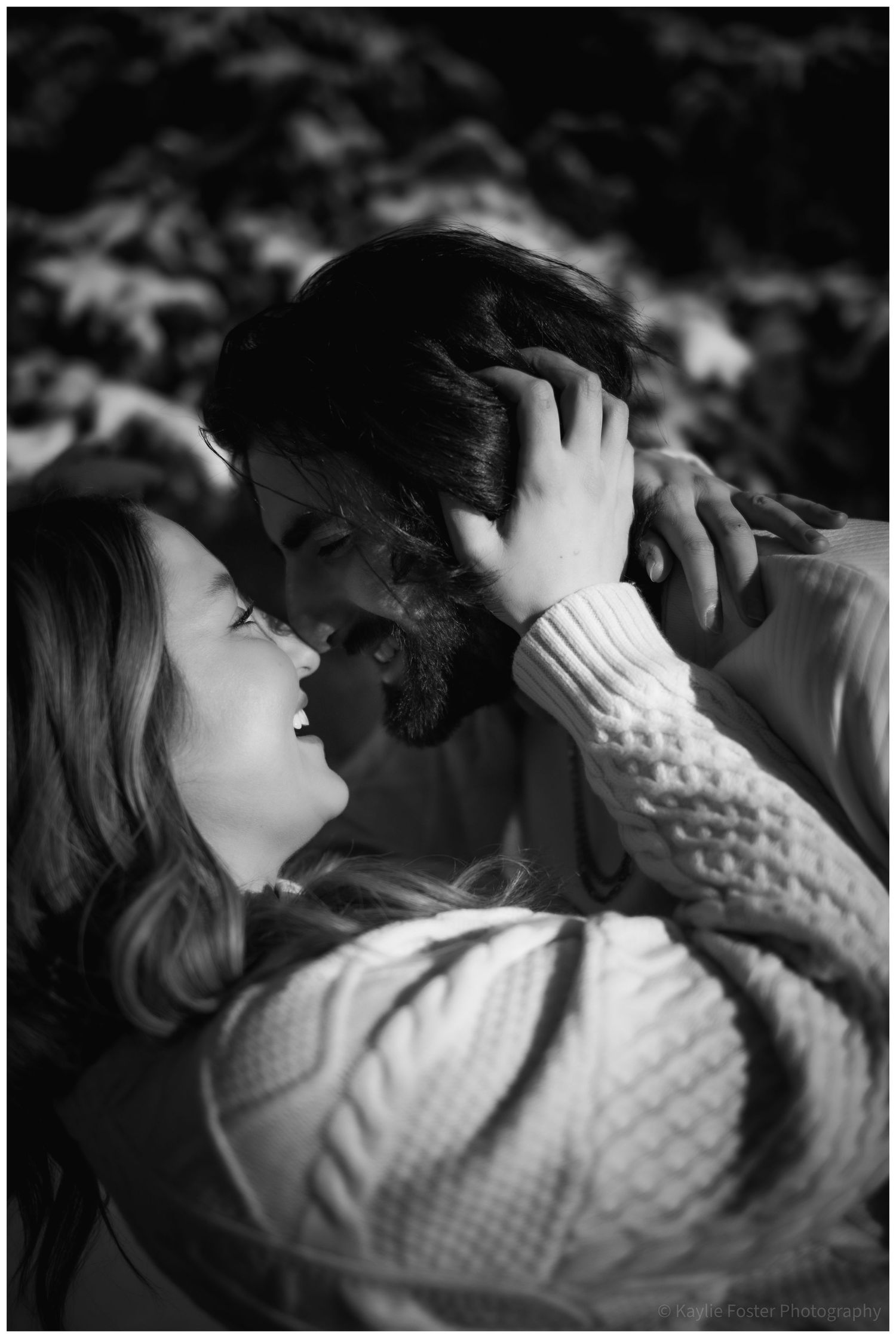 Black and white photo of a romantic couple sharing a tender moment, woman in cable knit sweater gently holding mans face.