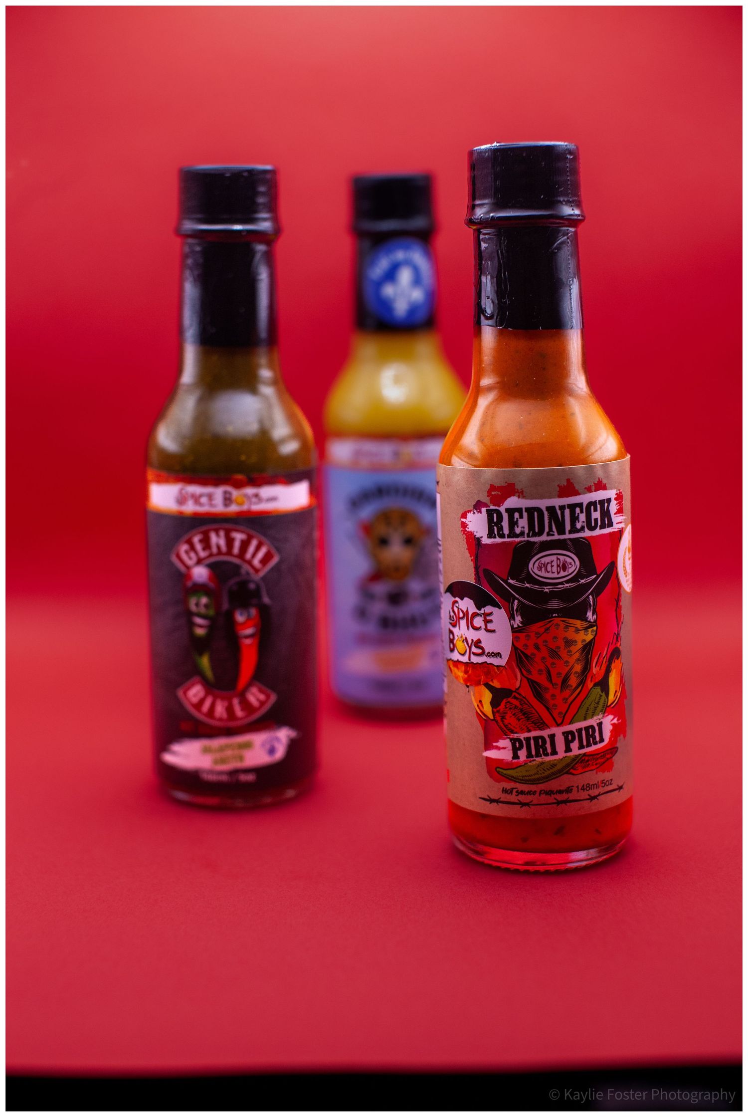 Redneck Piri Piri hot sauce in focus with Gentil Biker and Gardien D Bhut bottles on red background.