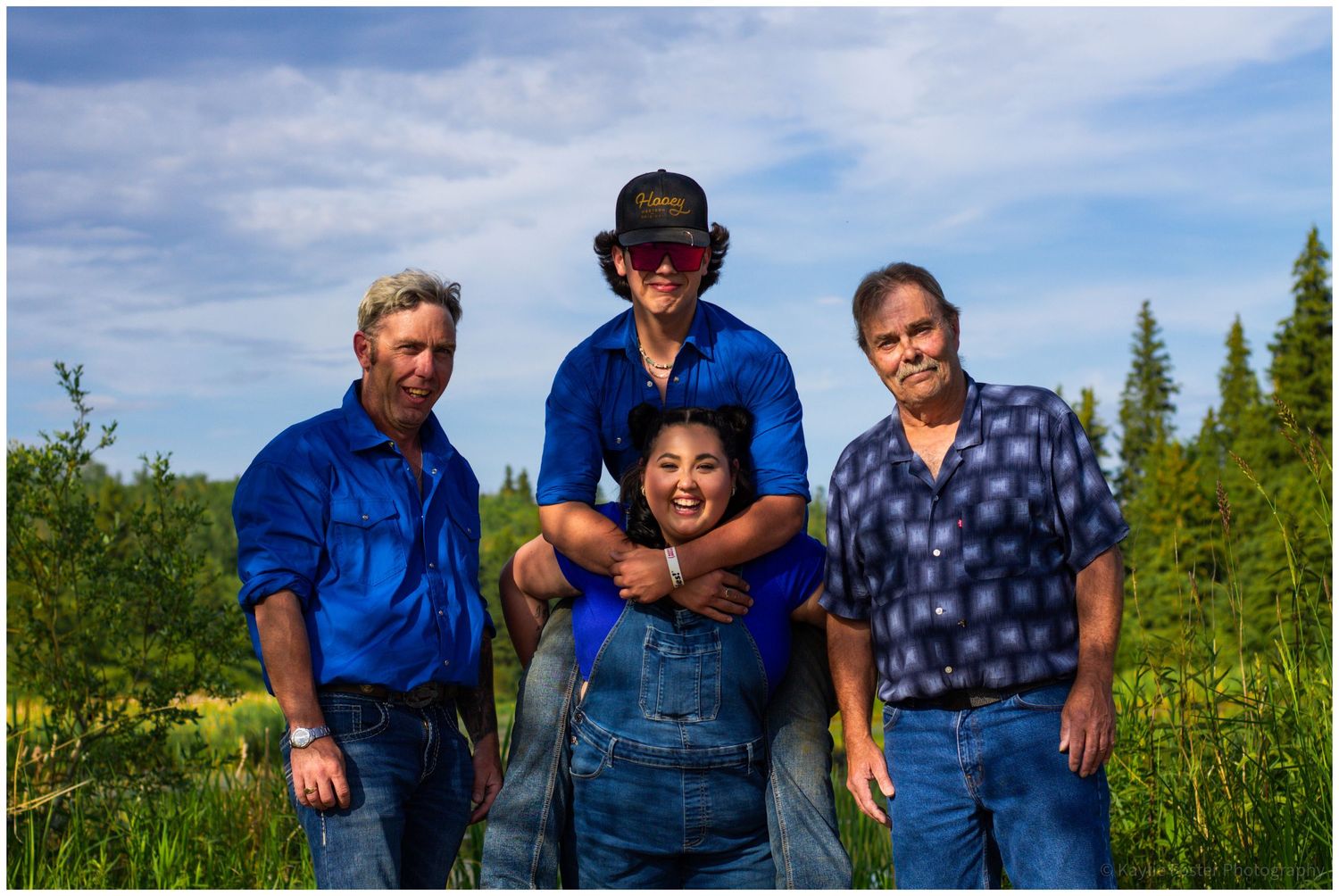 Group of four people posing outdoors, one person giving a piggyback ride in a green field.