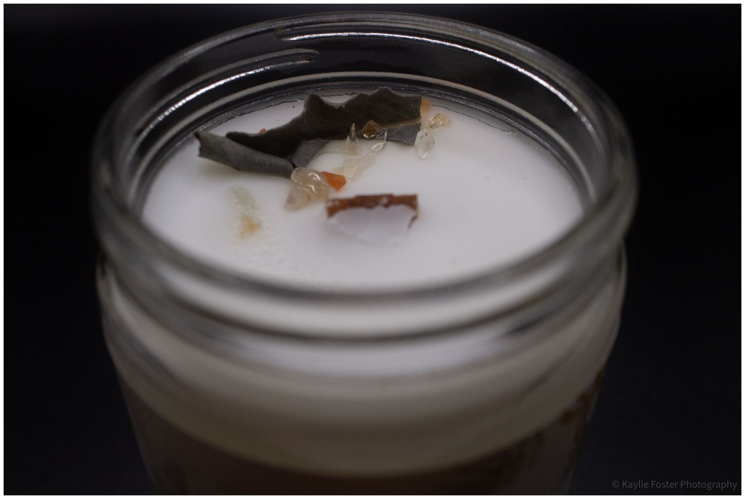Close-up top view of a hand-poured candle with wooden wick and dried botanicals in a glass jar.