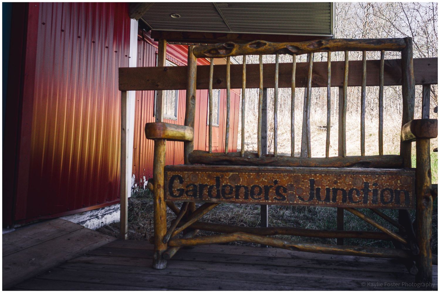 Rustic wooden bench with garden tools displayed at Gardeners Junction shop entrance on a wooden porch.