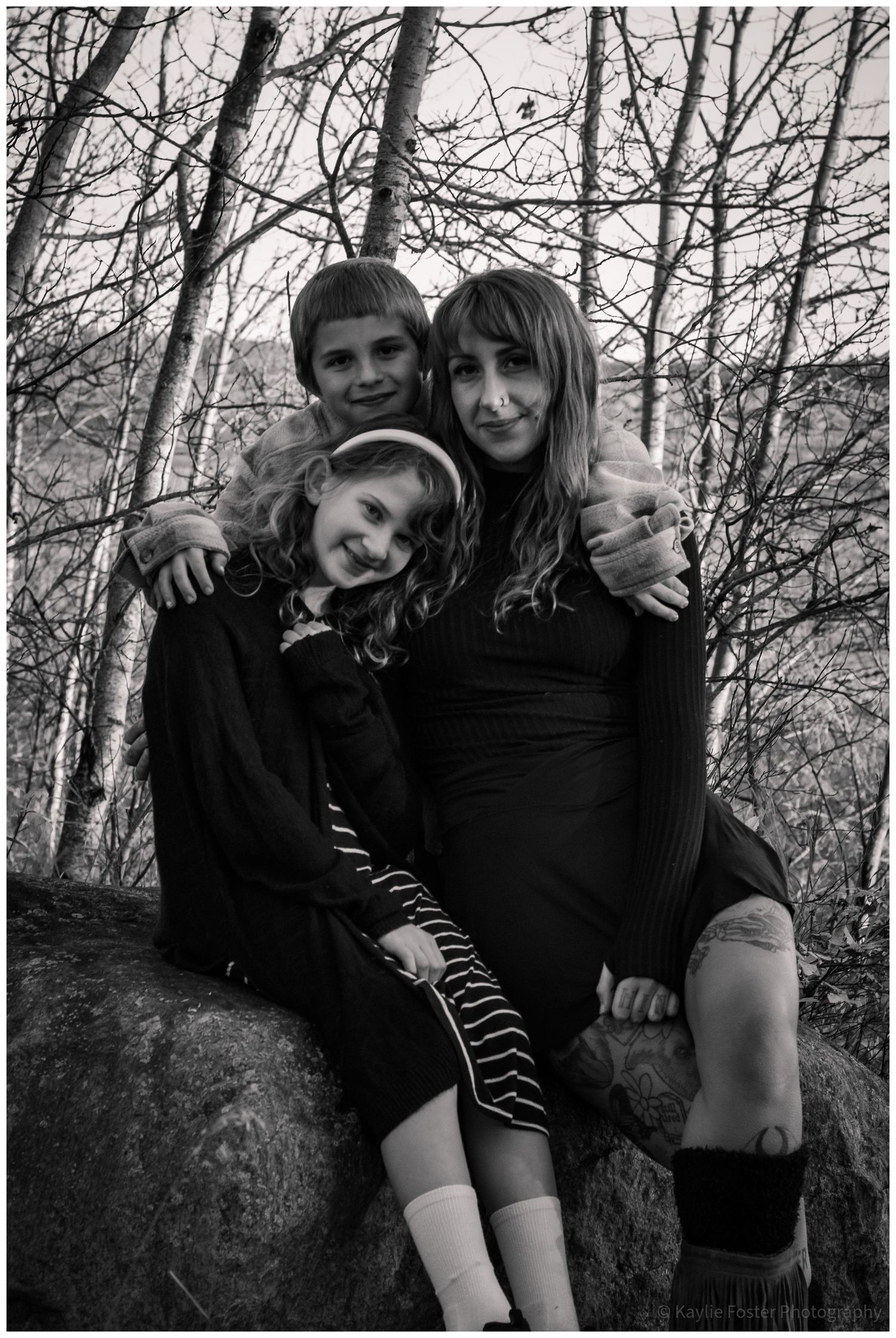 Black and white photo of a mother and two children sitting on rocks in a forest.