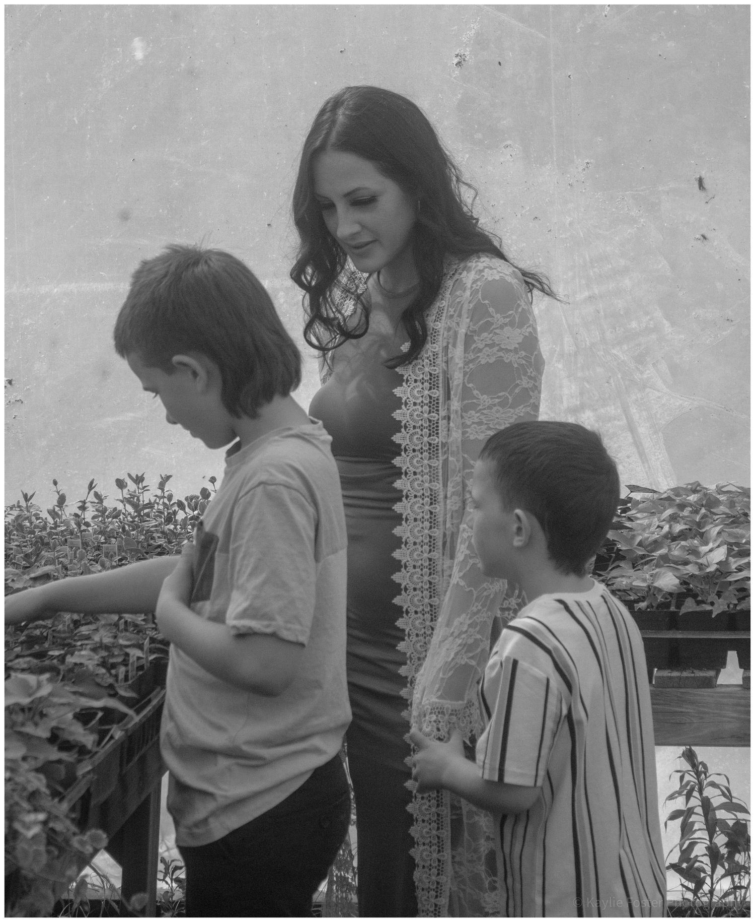 Black and white photo of a pregnant woman with two young boys in a garden.